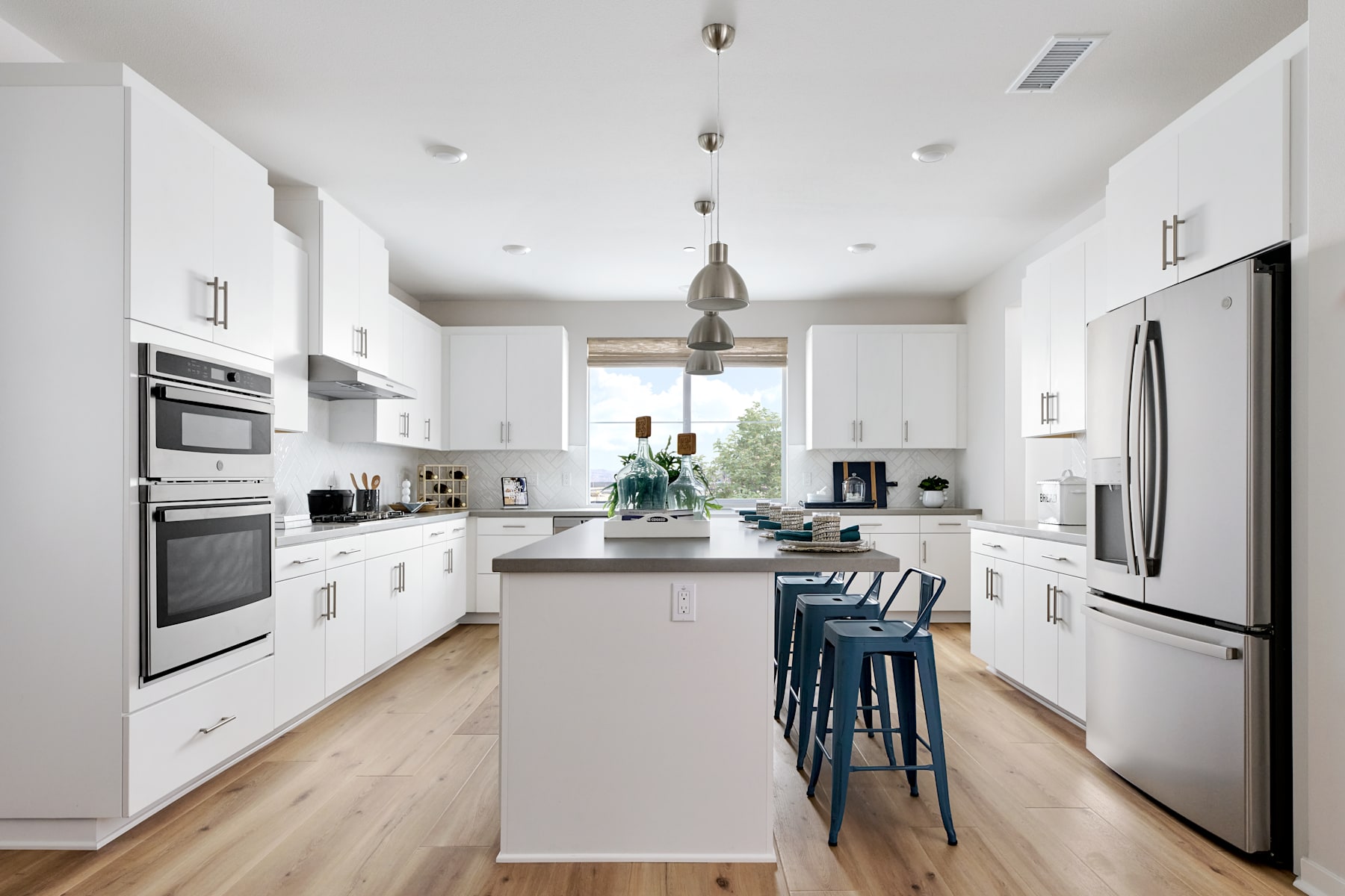 A modern, bright, and spacious kitchen with white cabinets, stainless steel appliances, and a central island with blue stools.