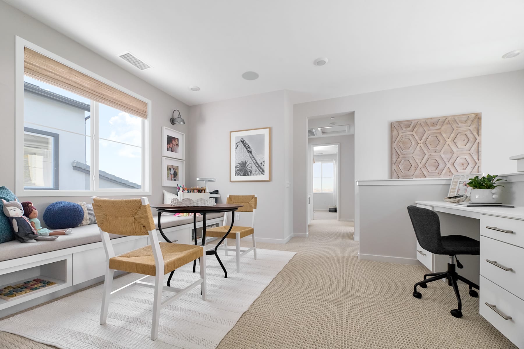 A bright and airy home office space with a wooden desk, comfortable chairs, and decorative accents, set against a backdrop of large windows and neutral-toned walls.