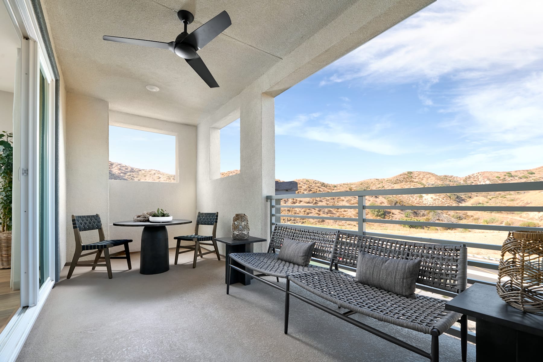A cozy outdoor patio with a ceiling fan, comfortable seating, and a stunning mountain landscape visible through the large windows, creating a serene and inviting atmosphere.