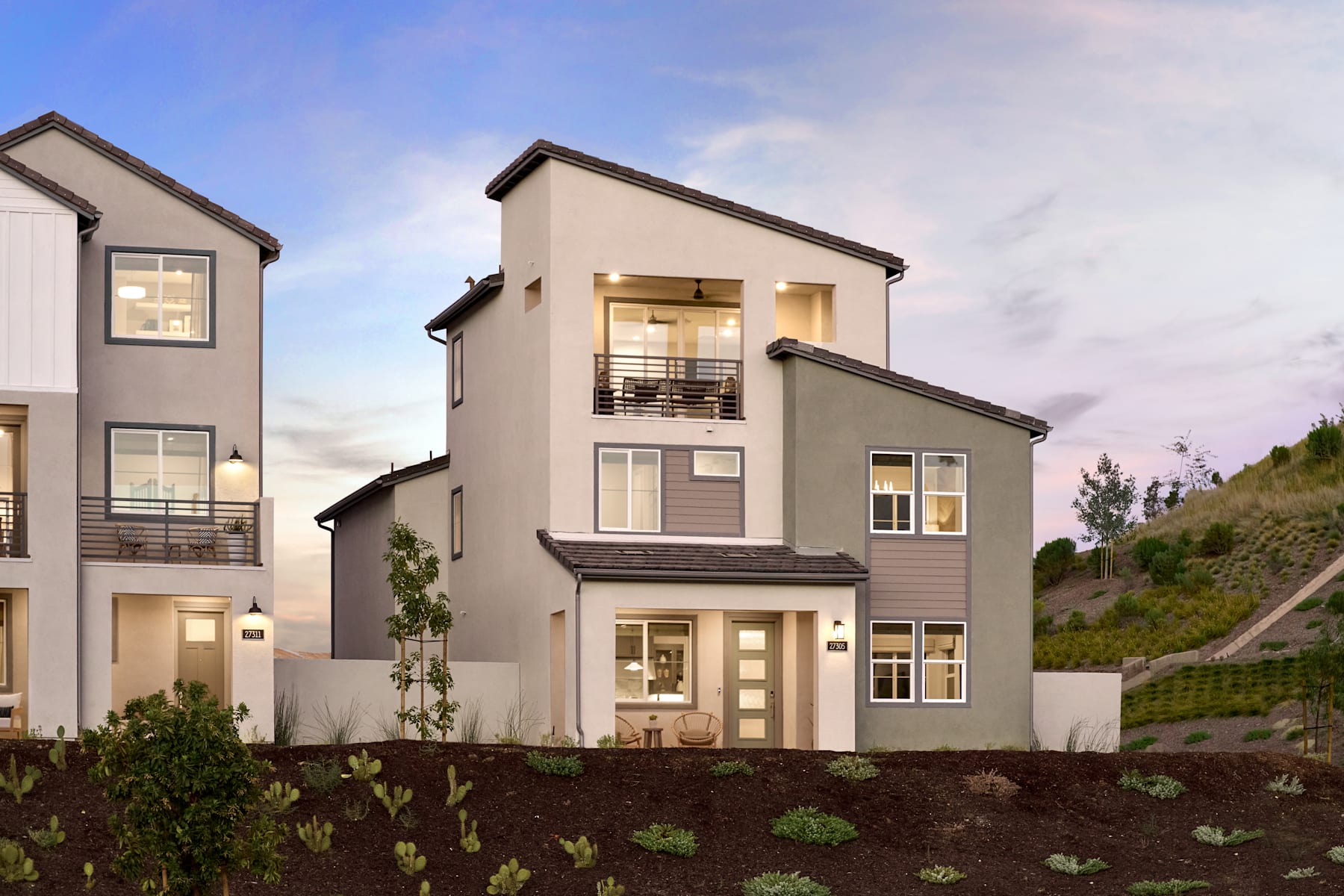 The image depicts a modern, multi-story residential building with a landscaped front yard and a clear blue sky in the background.