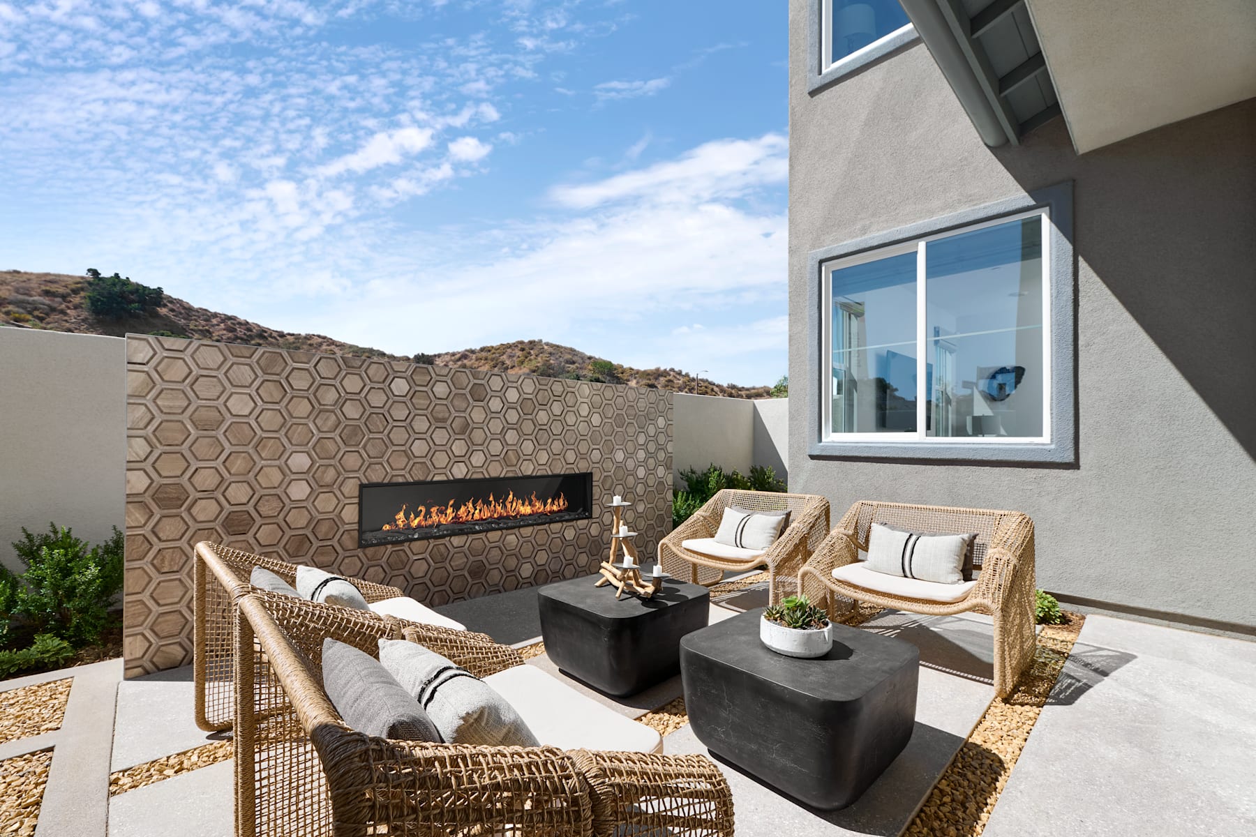 A cozy outdoor seating area with a fireplace, surrounded by a desert landscape and a modern building with large windows.