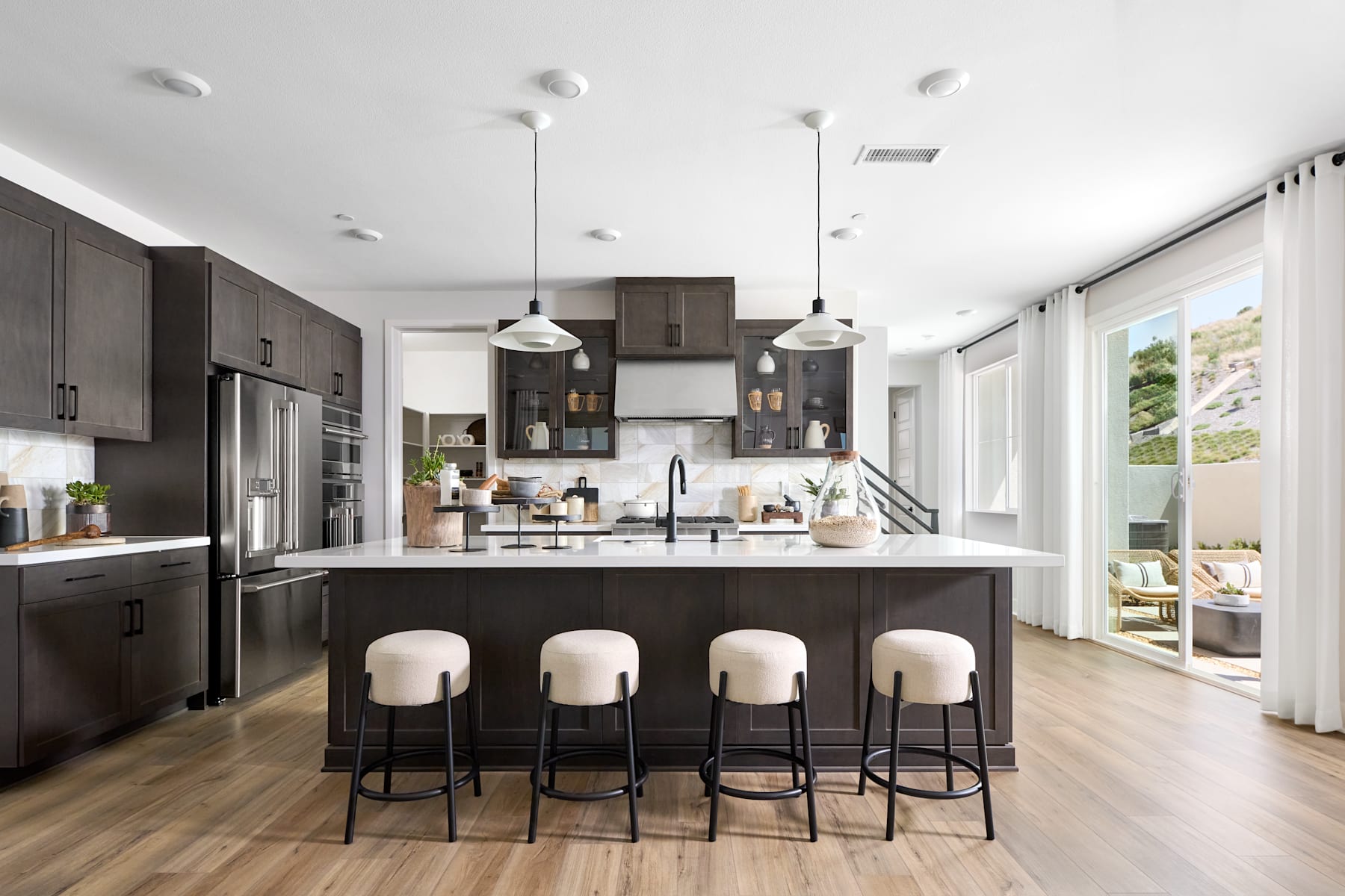 A modern and sleek kitchen with dark cabinets, a large island with bar stools, and a bright and airy atmosphere with large windows.