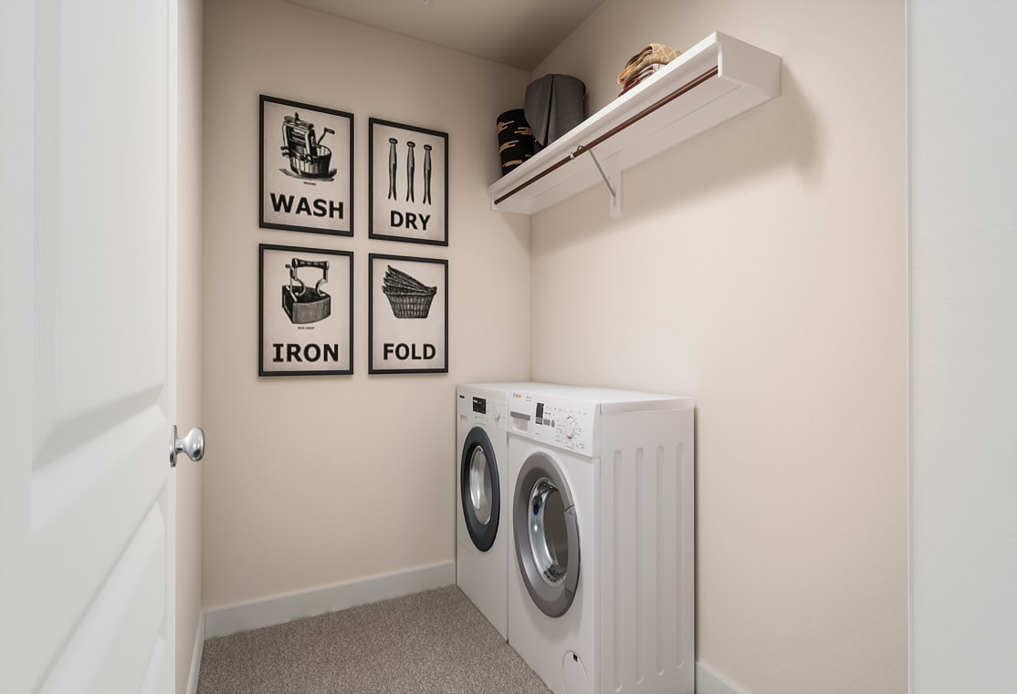 A small laundry room with a white washing machine, shelves, and wall decor featuring laundry-related icons and text.