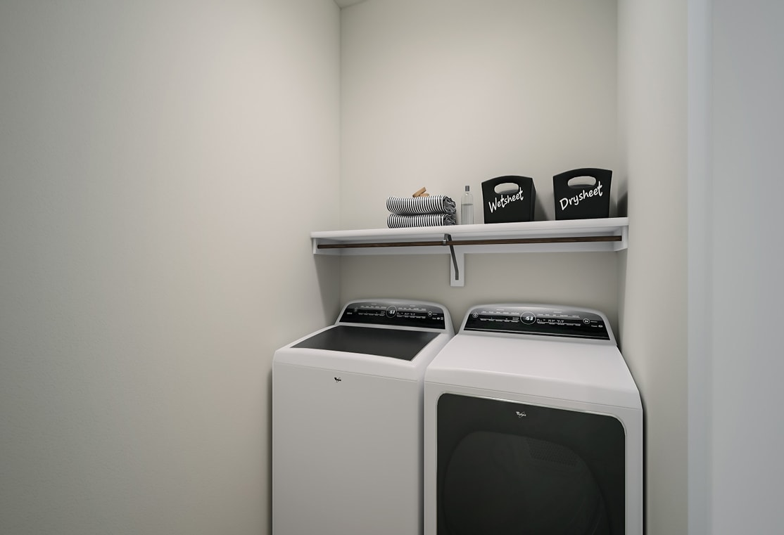 A small laundry room with a white washer and dryer, shelves above, and decorative items on the shelves.