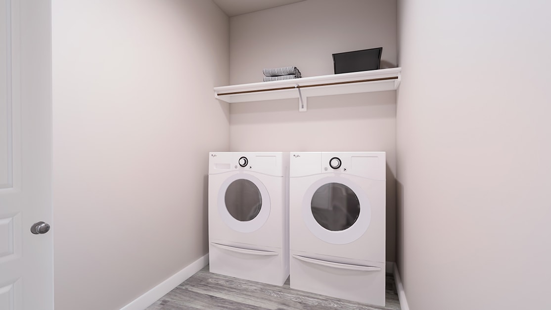 The image shows a laundry room with two white washing machines placed side by side, along with a shelf above them holding a small television or display.