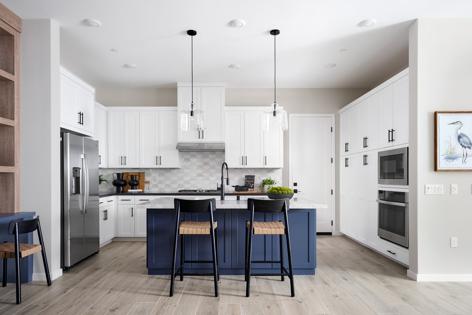 A modern, open-concept kitchen with white cabinets, stainless steel appliances, and a central island with navy blue stools.