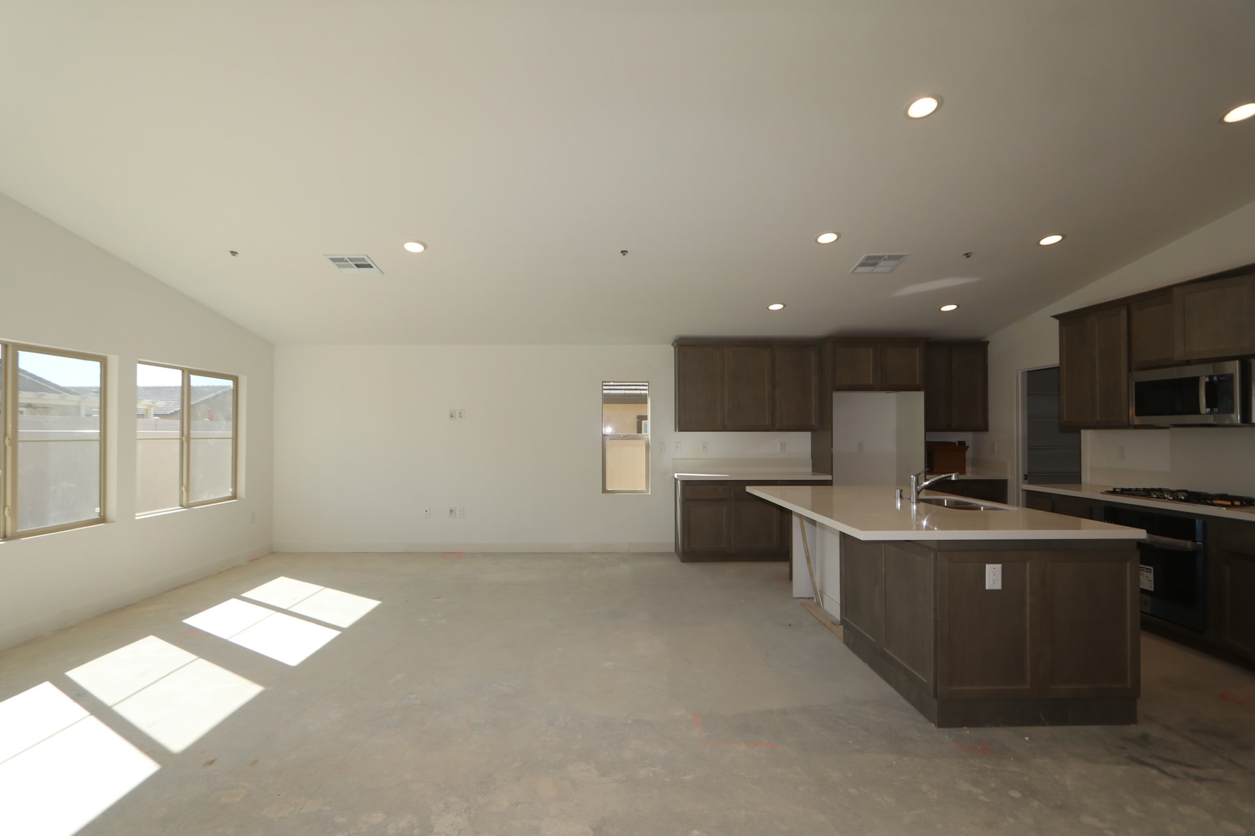 A spacious, modern kitchen with dark wood cabinets, a central island, and large windows allowing natural light to fill the open-concept living space.