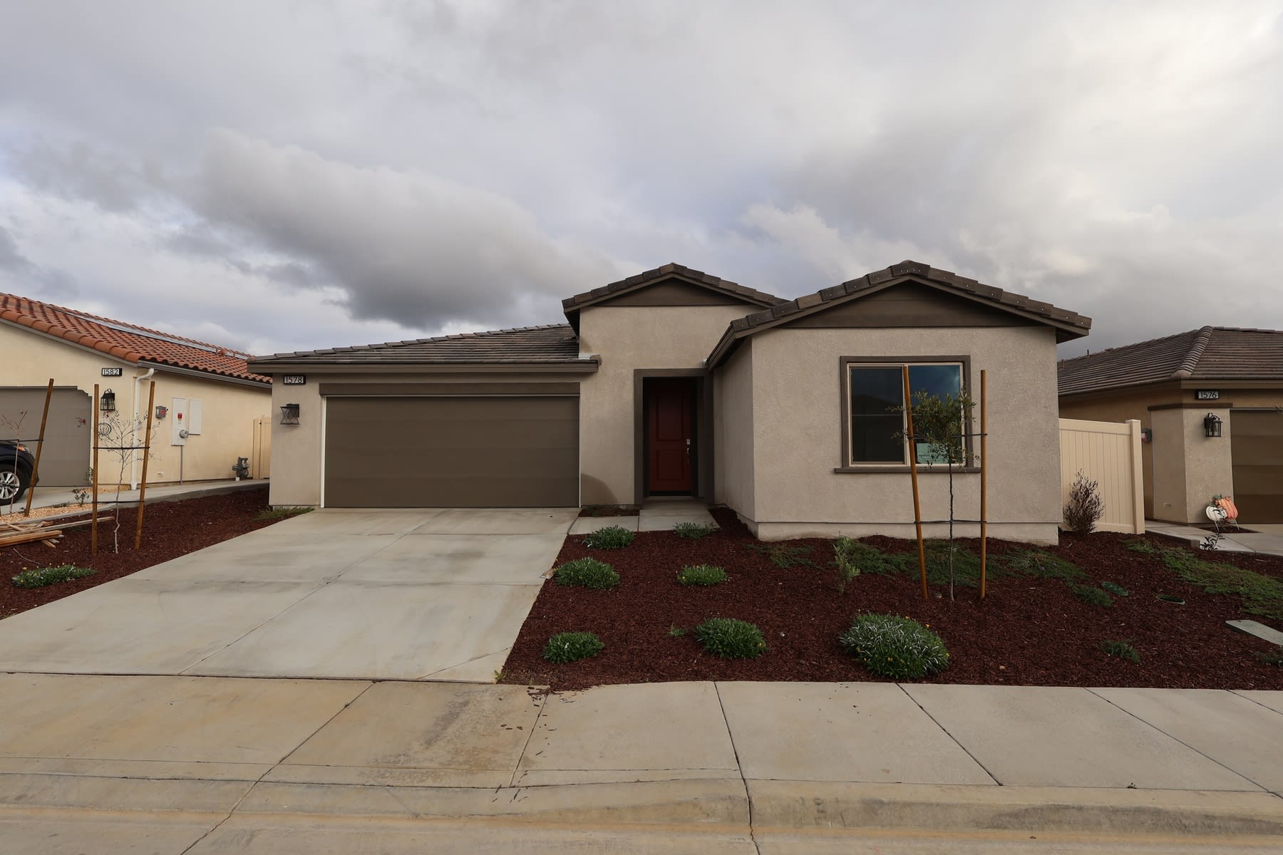 A modern, single-story house with a tiled roof, surrounded by a landscaped yard with a concrete walkway leading to the entrance.