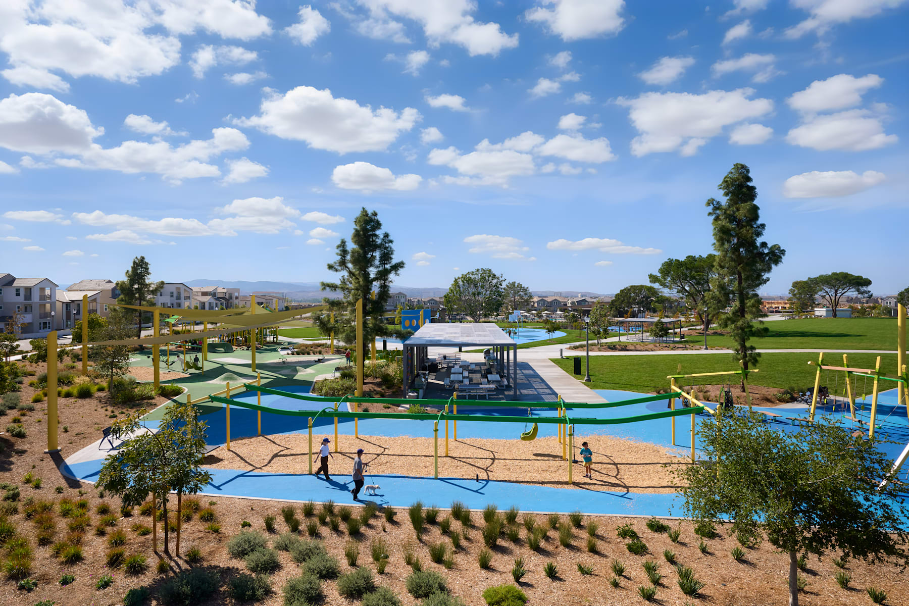 A vibrant outdoor recreational area with a colorful water park, surrounded by lush greenery and a clear blue sky dotted with fluffy white clouds.