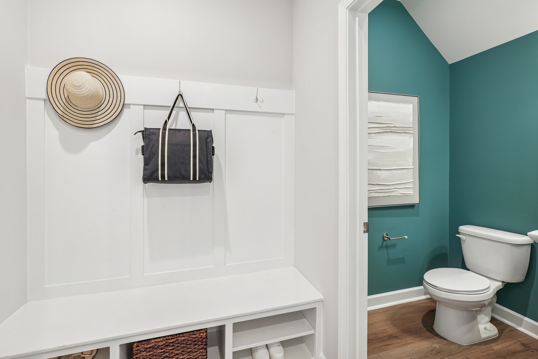 A modern and minimalist bathroom with a white bench, a hanging bag, and a teal-colored wall in the background.