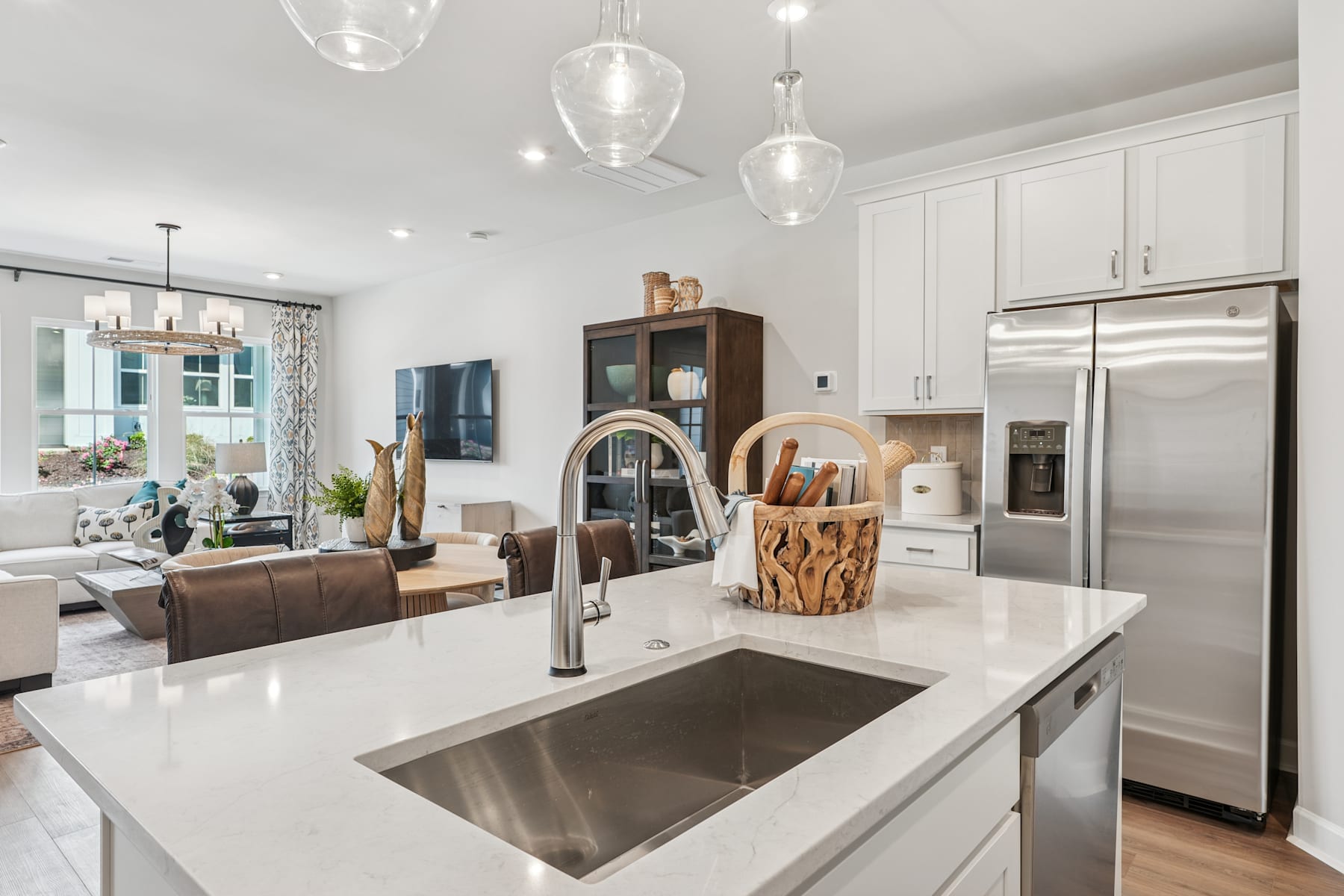 A modern, open-concept kitchen with a large island, stainless steel appliances, and pendant lighting, set against a backdrop of a living room area with a leather sofa and decorative accents.