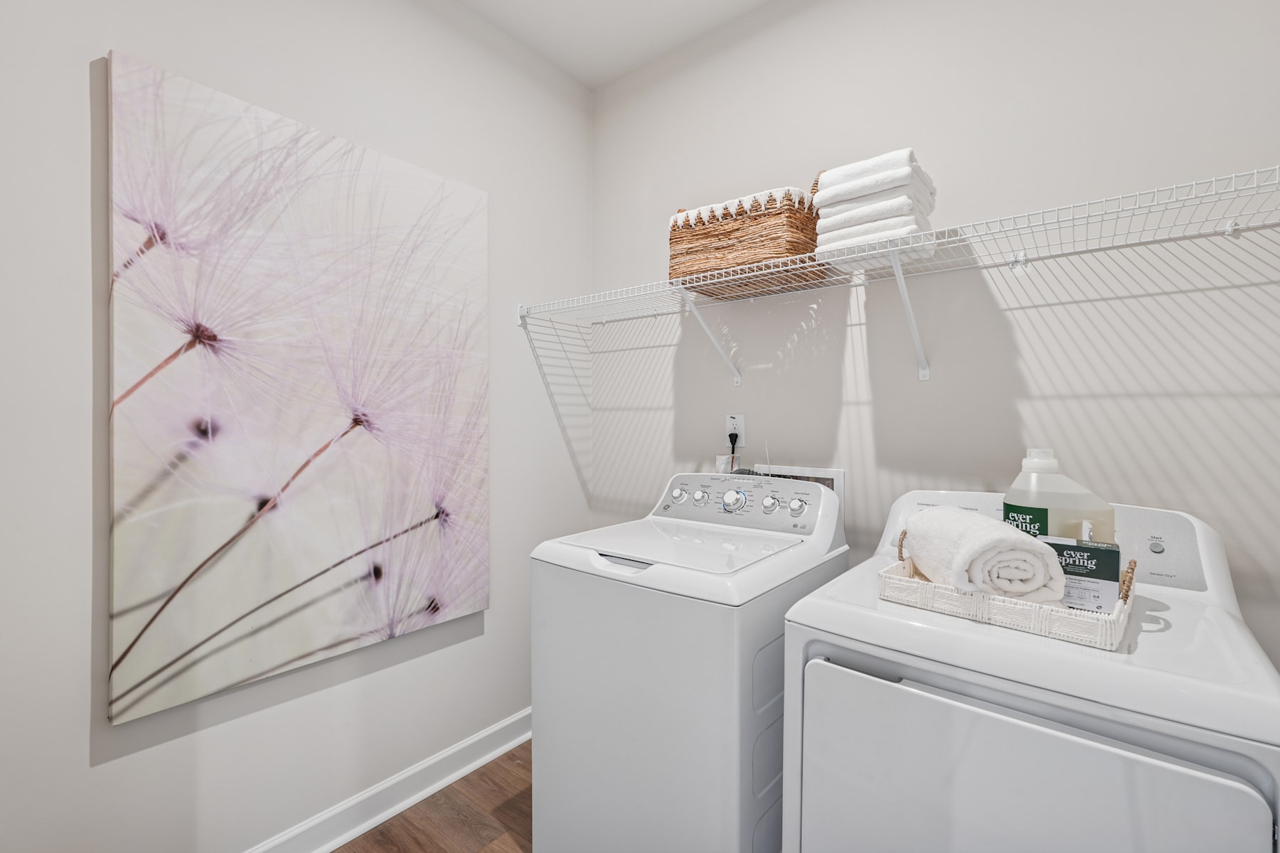 A bright and airy laundry room with a floral artwork on the wall, a washing machine, and a dryer, along with various storage and organizational items.
