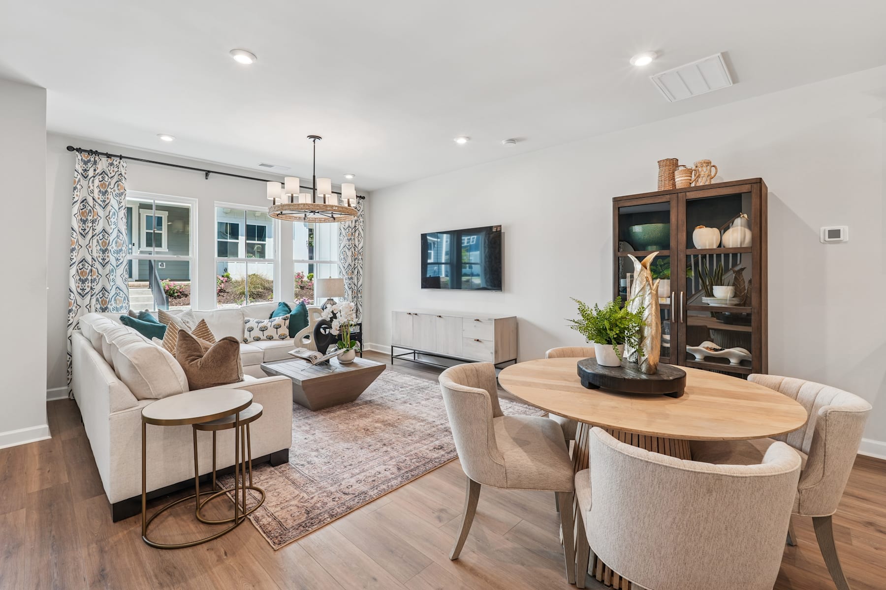 A cozy and well-designed living room with a dining area, featuring a mix of modern and rustic elements, including a wooden dining table, plush seating, and a decorative display cabinet.