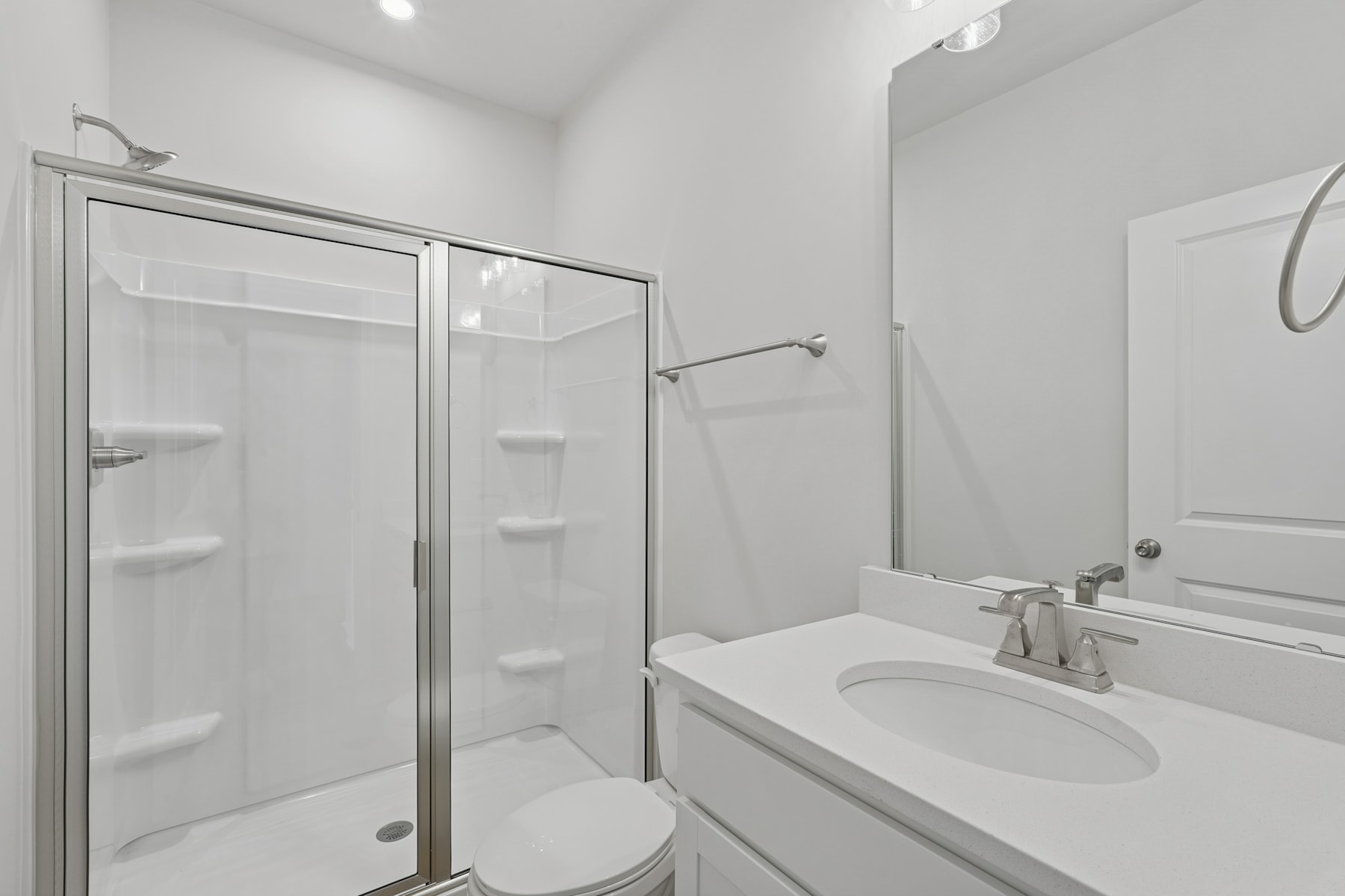 A modern, minimalist bathroom with a glass-enclosed shower, a white vanity, and a mirror on the wall.