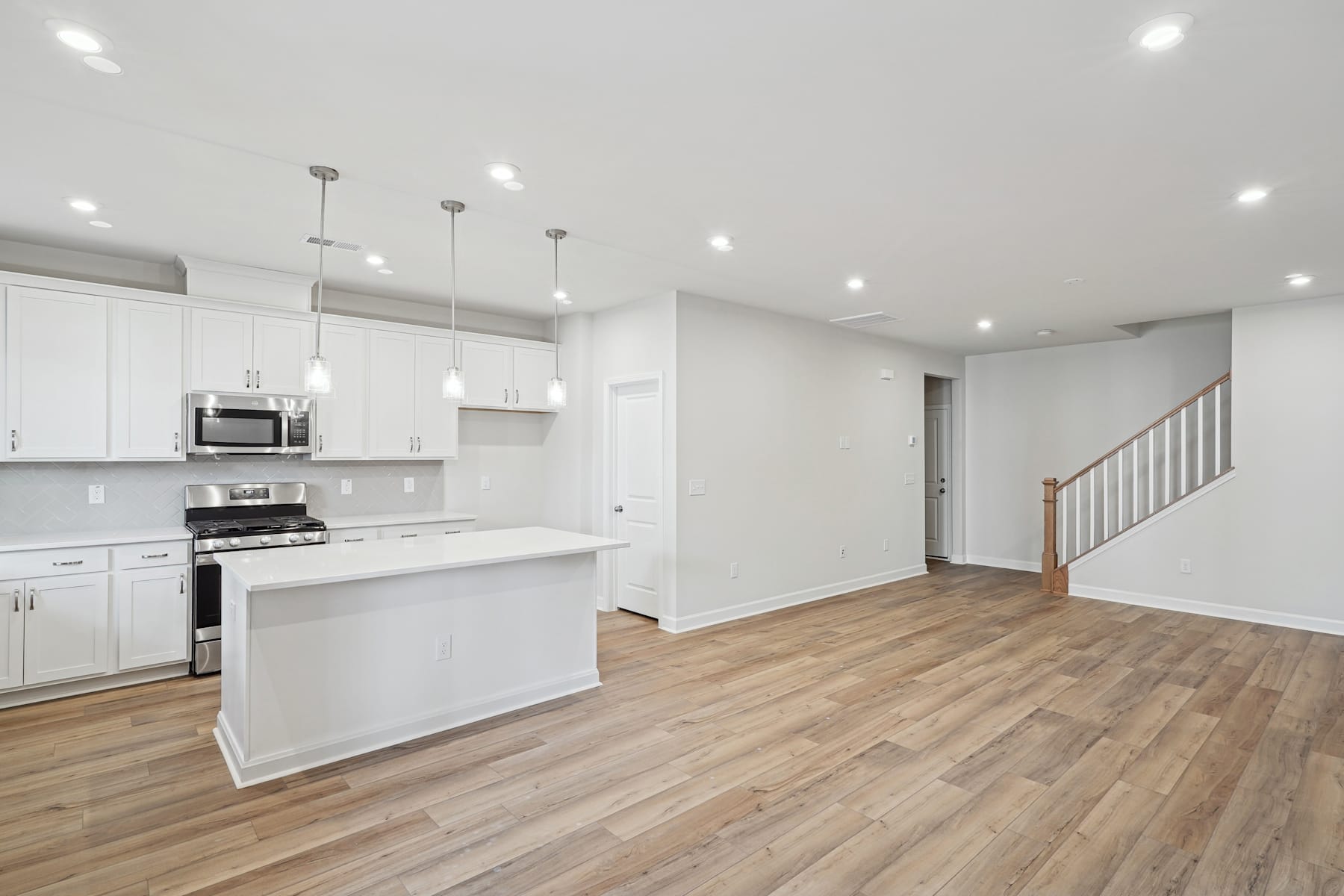 A modern, open-concept kitchen and living space with white cabinets, hardwood floors, and pendant lighting.