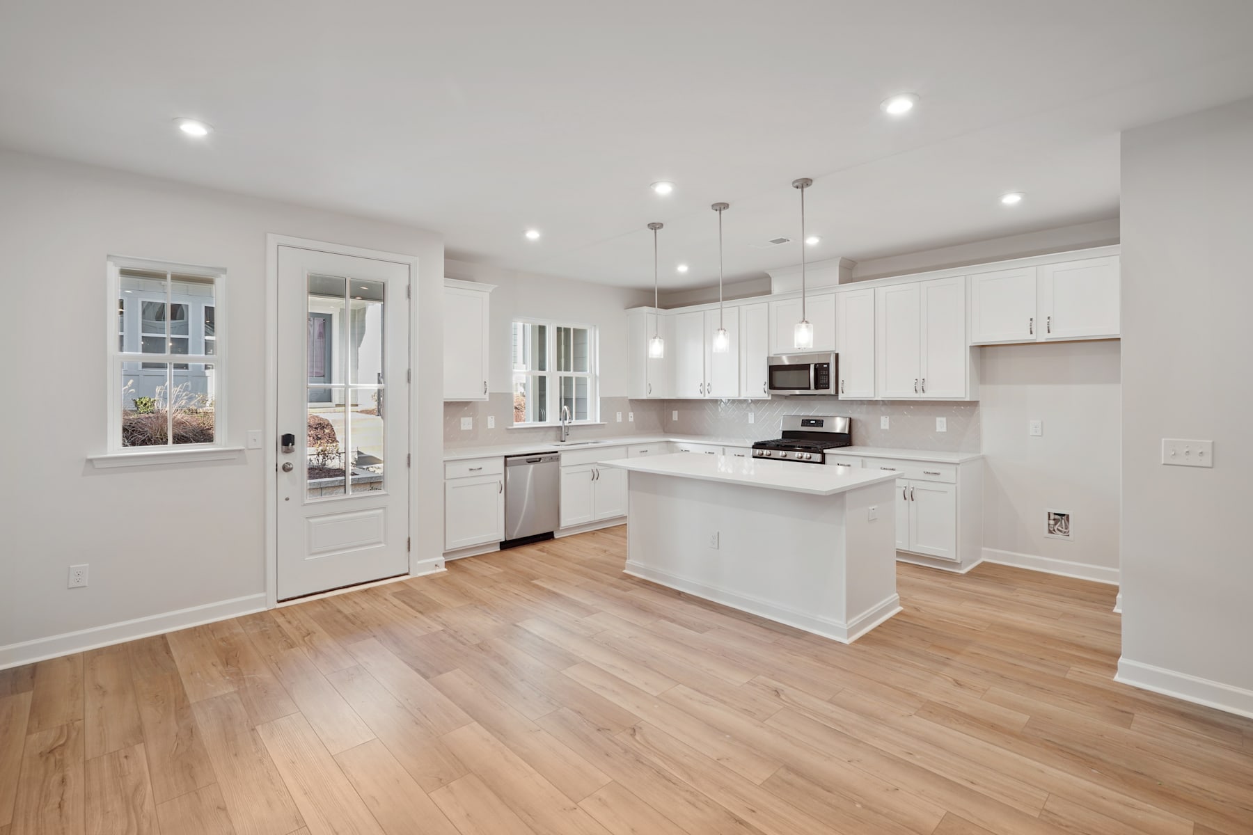A modern, bright kitchen with white cabinets, hardwood floors, and pendant lighting fixtures.