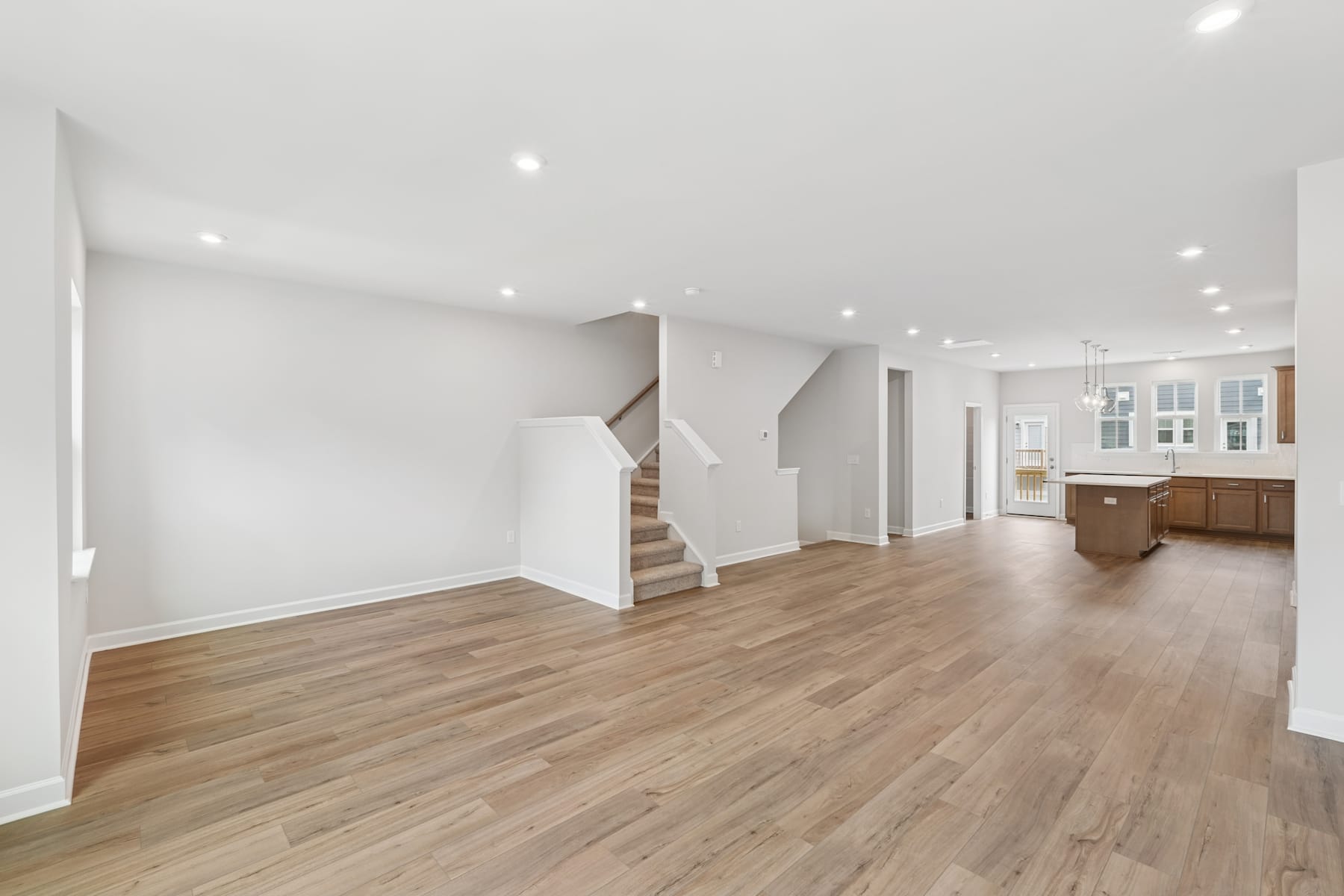 A spacious, open-concept living area with white walls, hardwood floors, and a kitchen visible in the background.