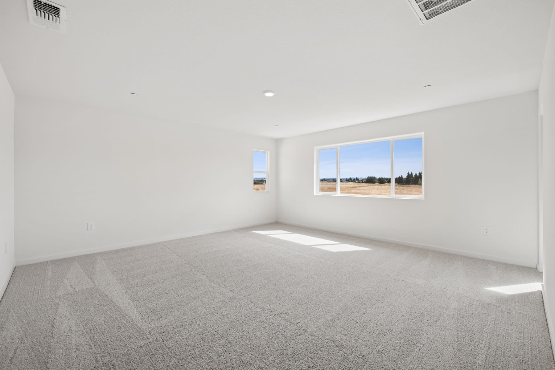 An empty, bright room with large windows overlooking a scenic outdoor landscape.