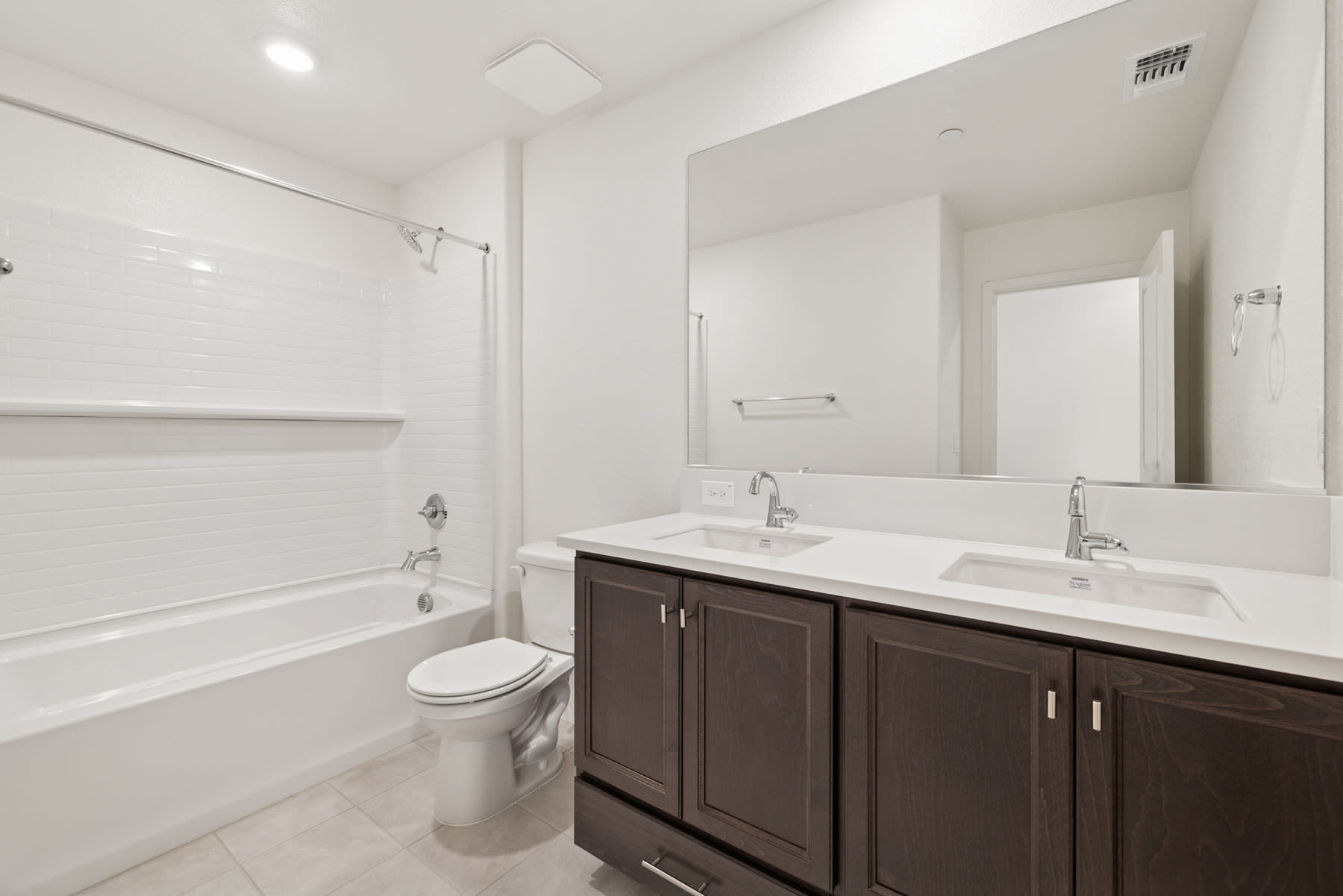 A modern, well-lit bathroom with a double vanity, a toilet, and a bathtub visible in the background.
