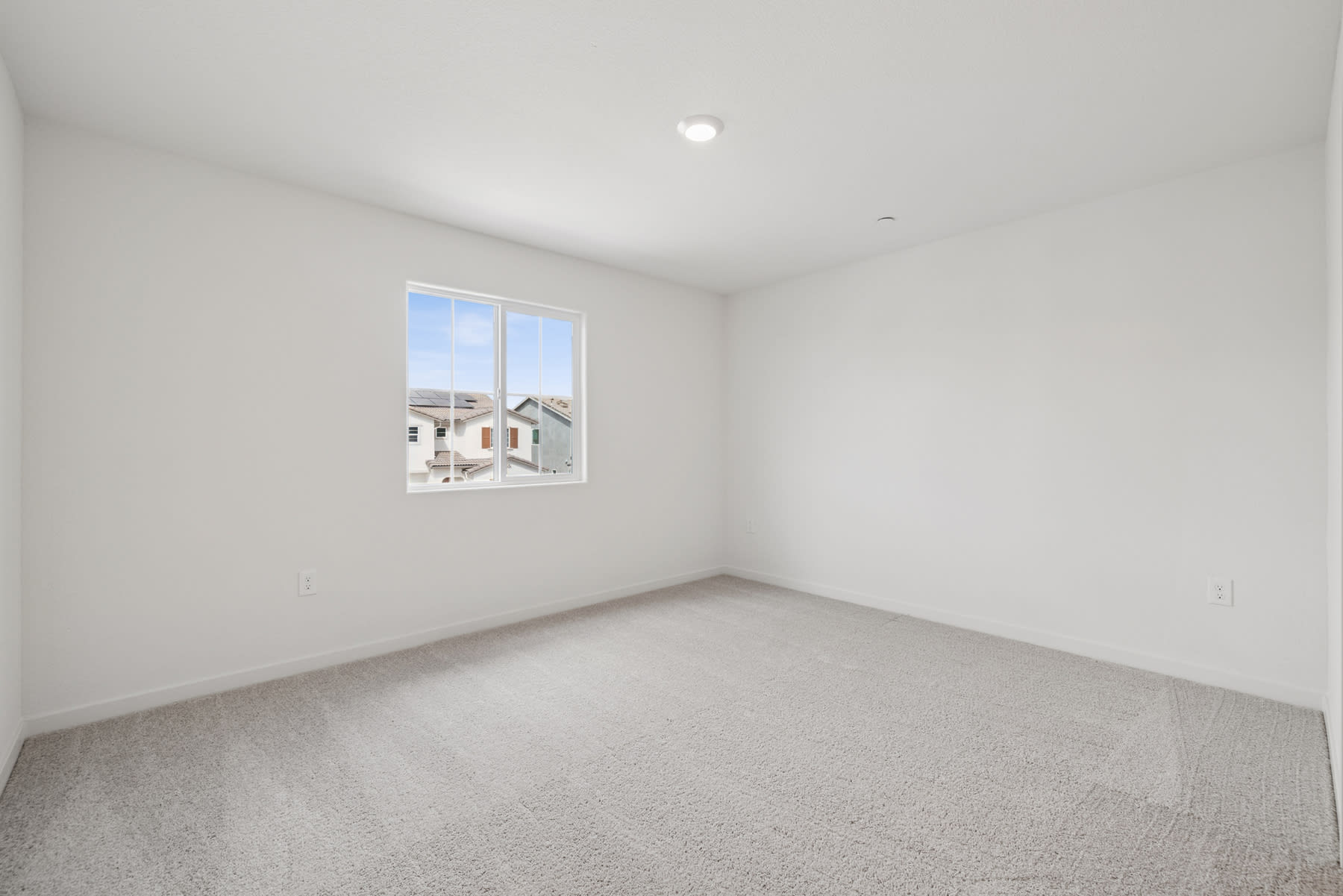 A simple, empty room with a window overlooking a residential neighborhood in the background.