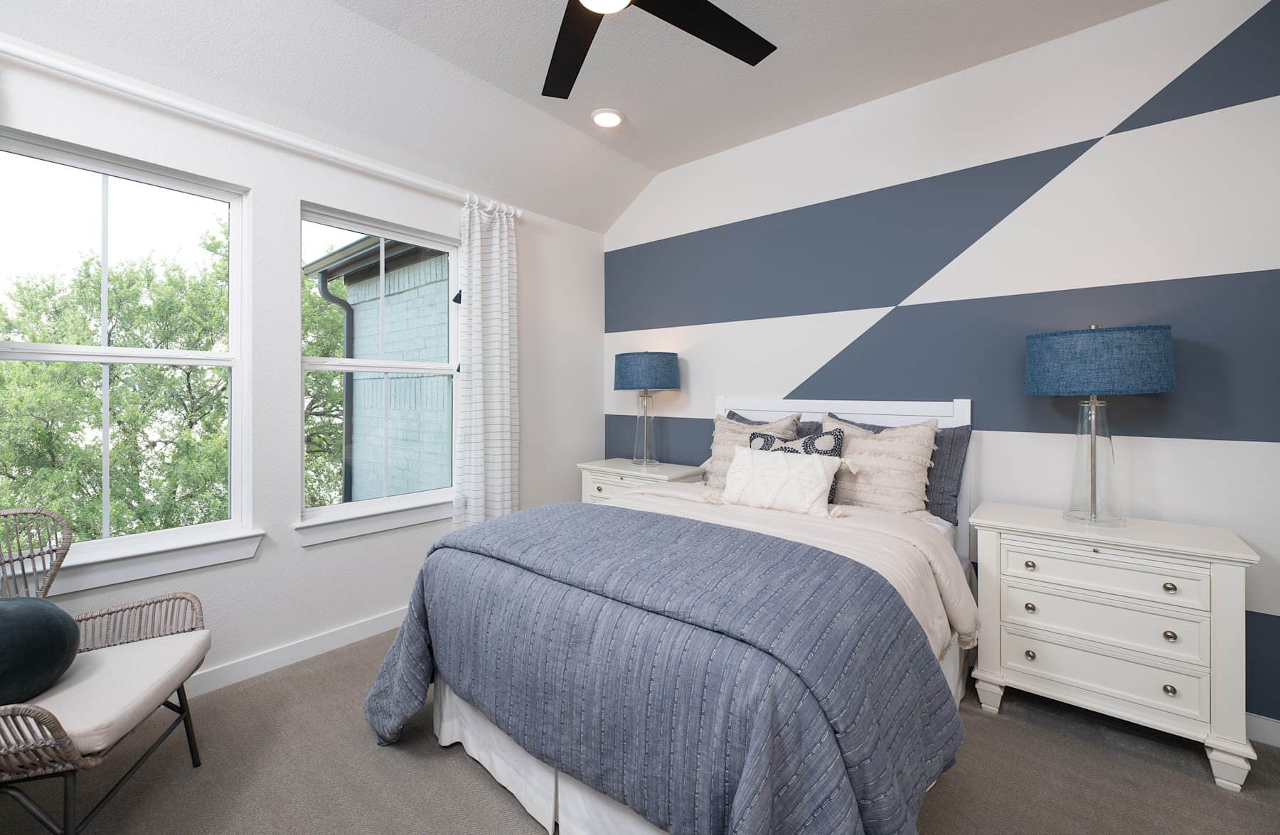 A modern and stylish bedroom with a large window, featuring a gray and white color scheme, a plush bedding set, and decorative lamps on the nightstands.