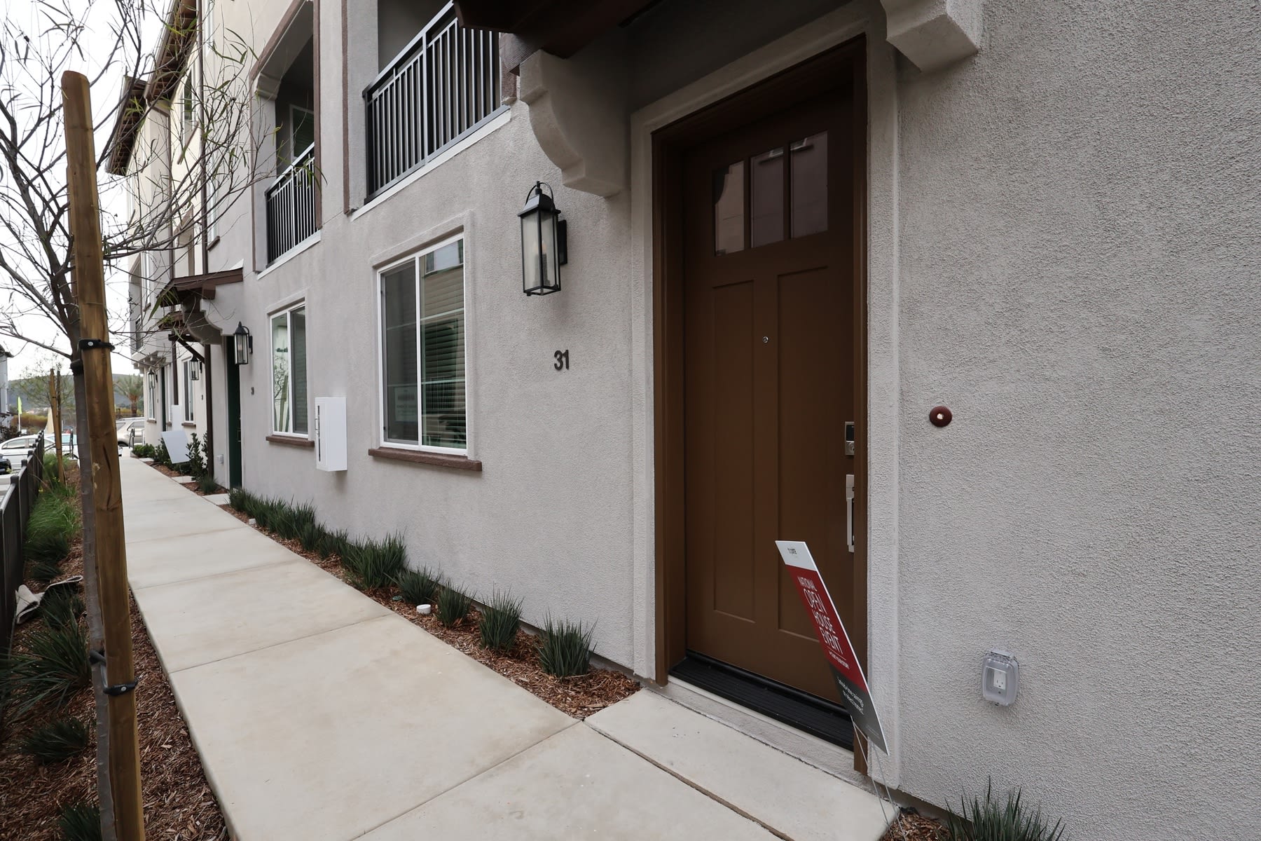 A residential building with a wooden door, surrounded by a concrete walkway and landscaping, stands in a quiet urban setting.