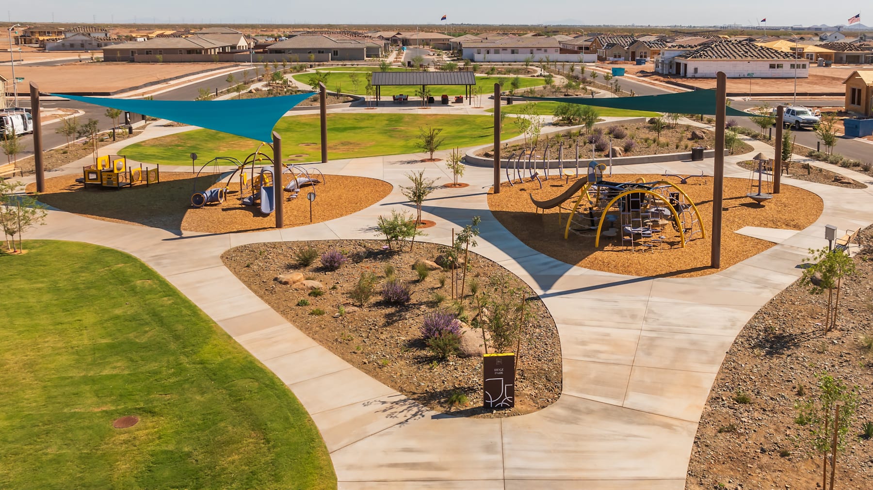 A vibrant and well-designed outdoor recreational area with various play structures, shaded seating areas, and lush landscaping, set against a backdrop of residential buildings.