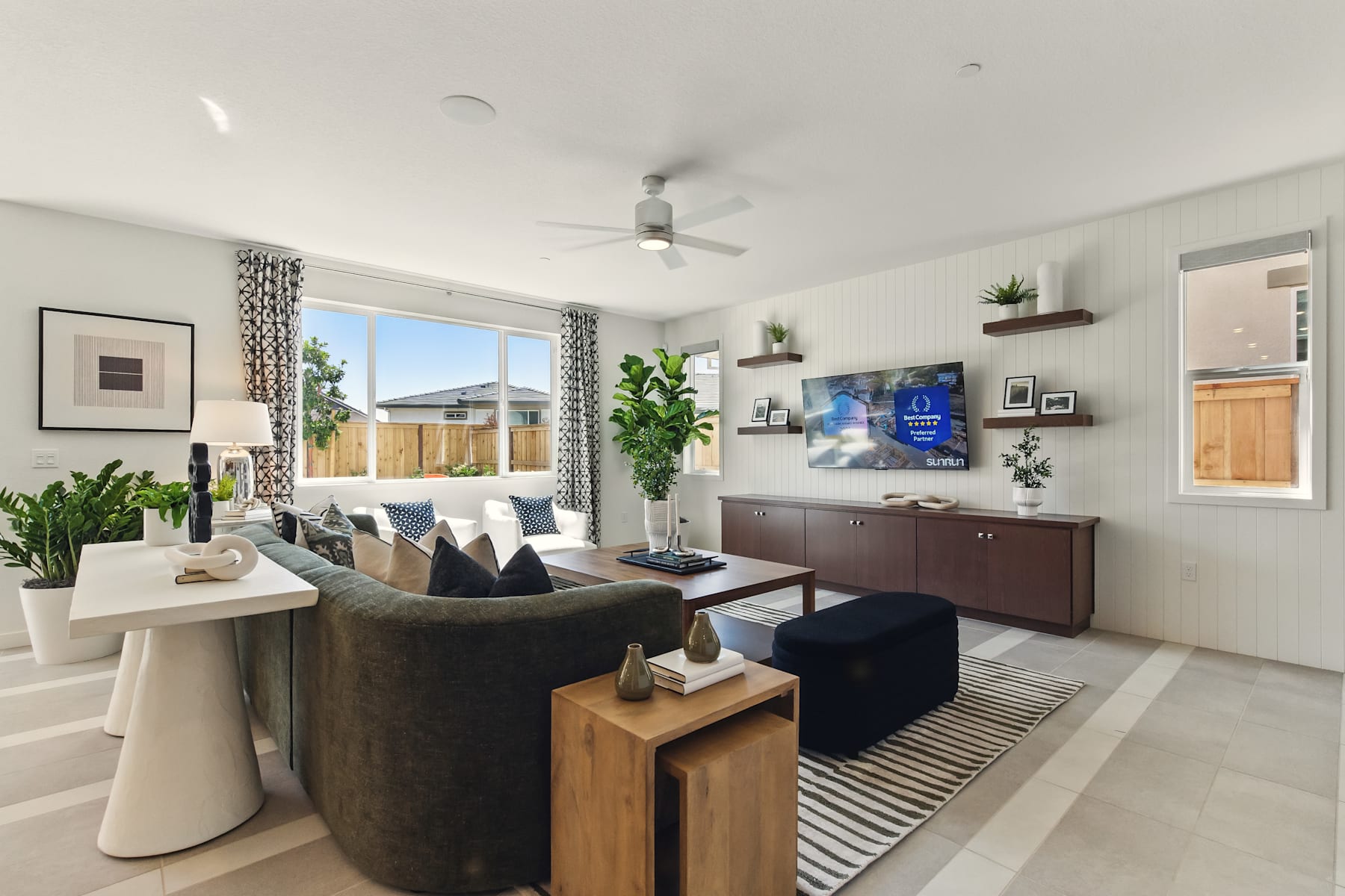 A modern and stylish living room with a large sofa, a wooden TV stand, and various decorative elements such as plants and artwork on the walls.