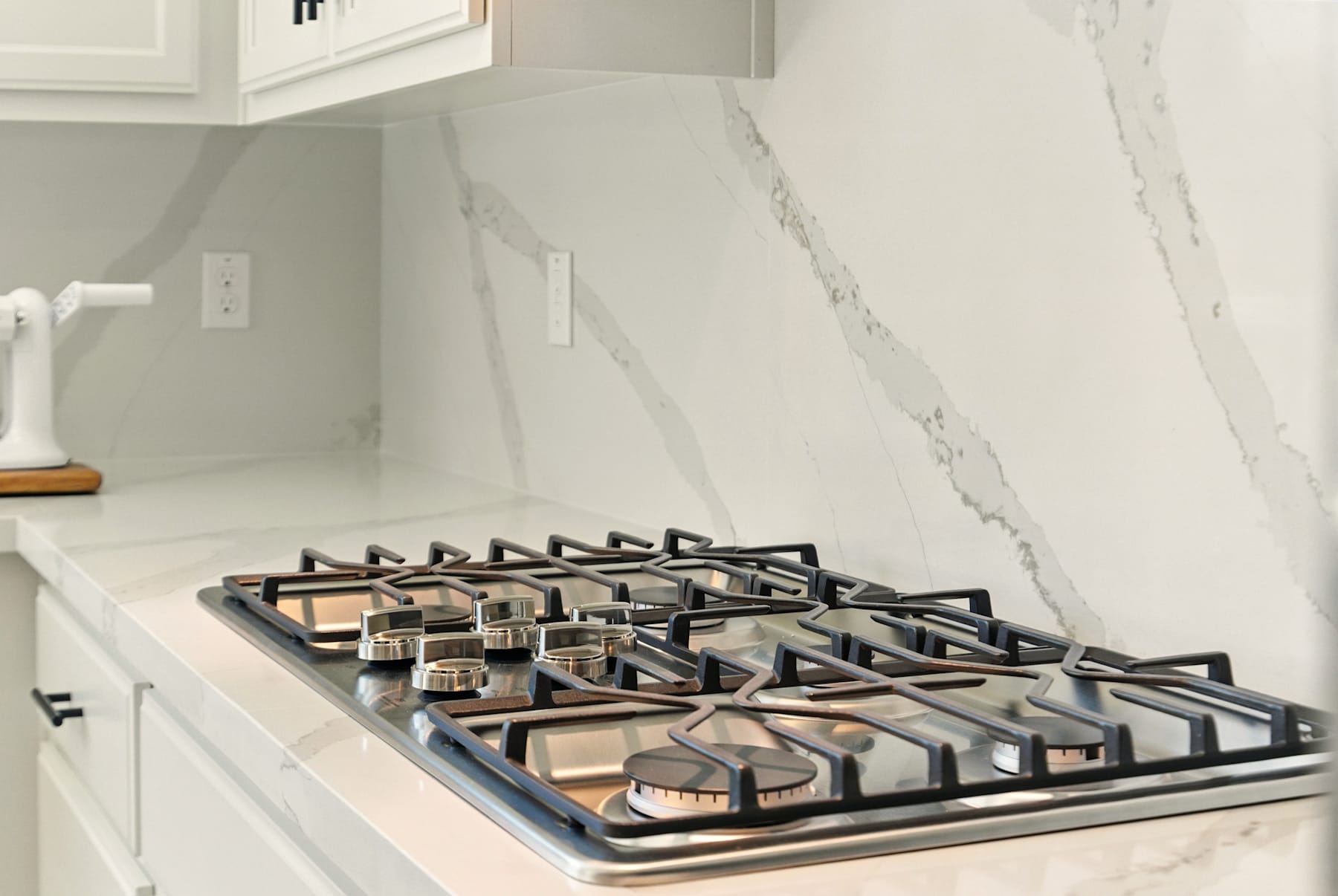 A modern gas stove with a sleek, black surface sits on a marble countertop in a bright, minimalist kitchen.