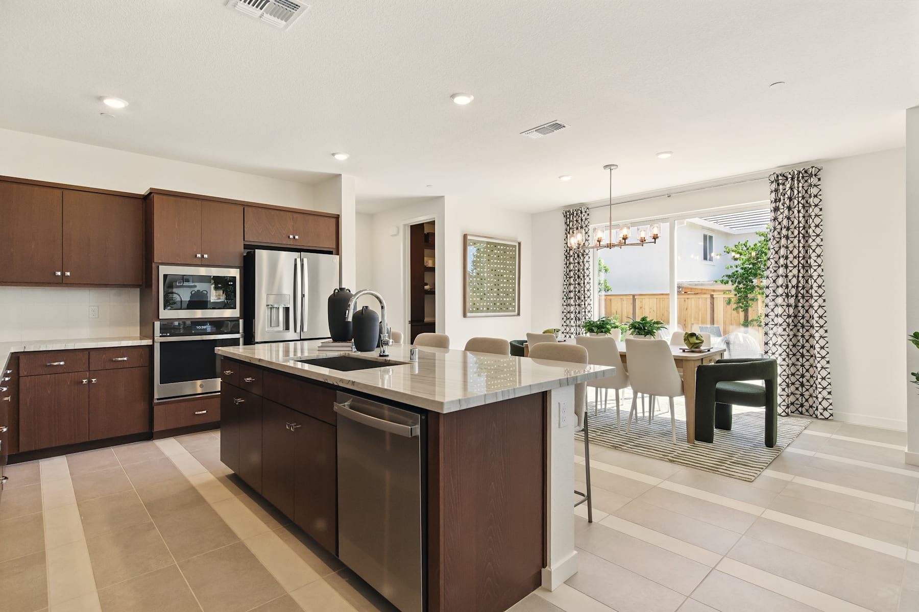 A modern and spacious kitchen with dark wood cabinets, stainless steel appliances, and a large central island with a granite countertop, surrounded by a dining area with a table and chairs.