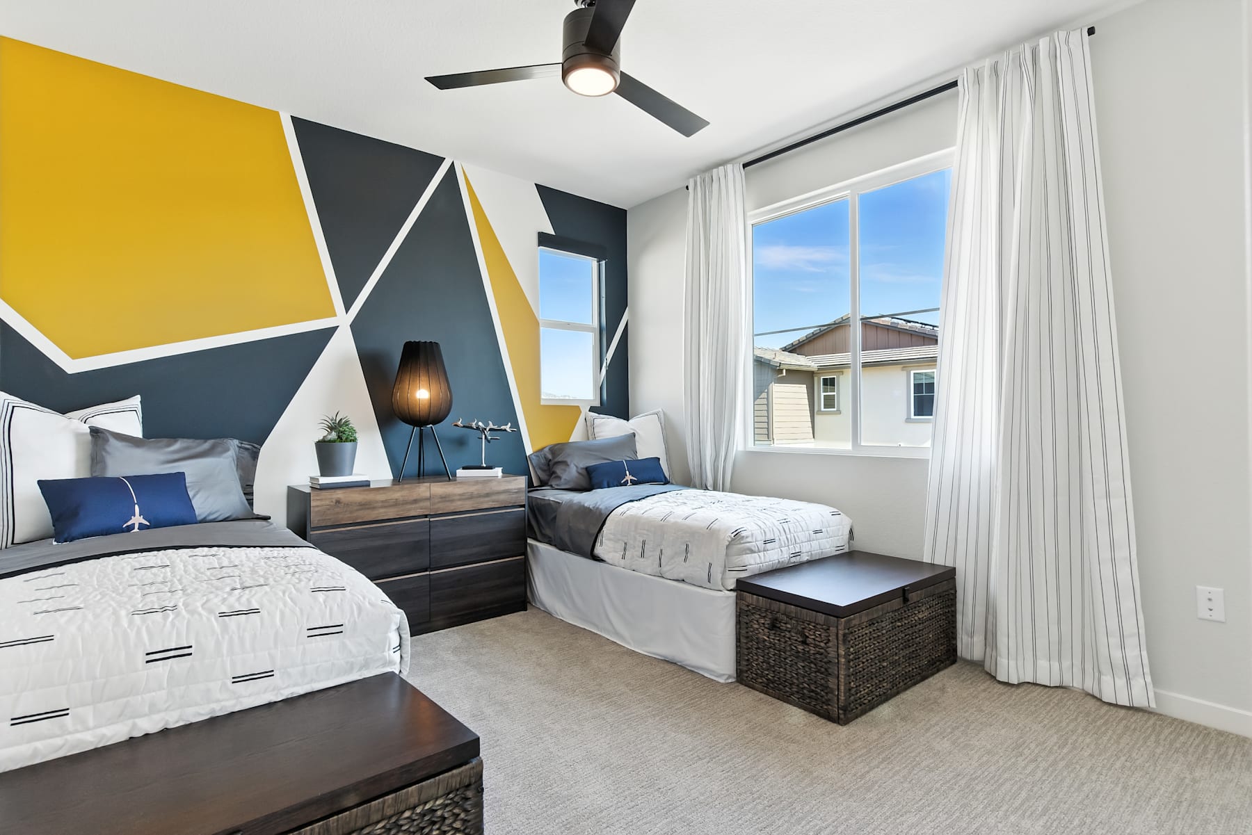 A modern and stylish bedroom with geometric wall patterns in shades of yellow, gray, and blue, featuring a large window overlooking a scenic outdoor view.