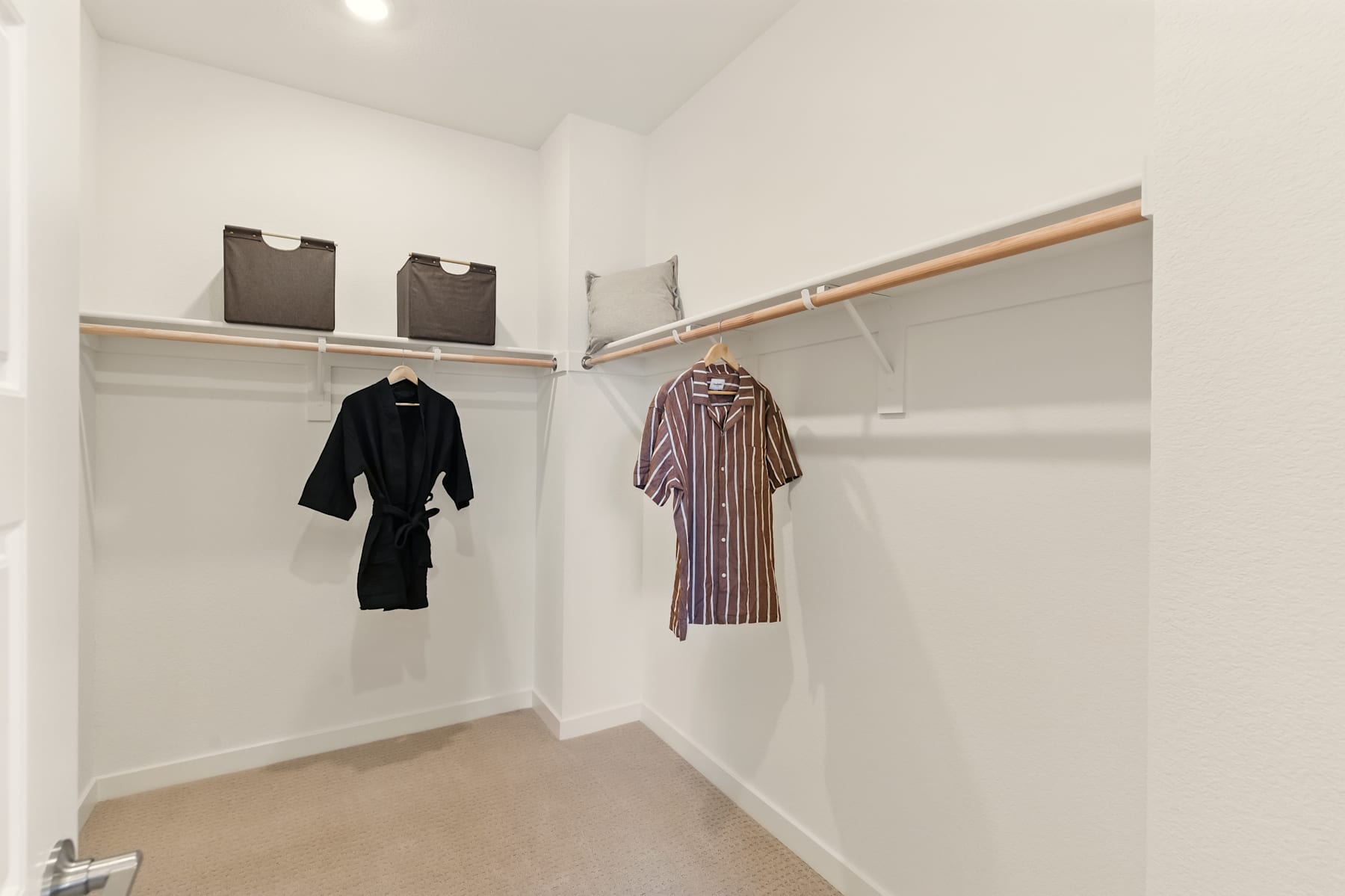 A well-organized closet with hanging clothes, shelves, and a clothing rod, providing ample storage space in a clean, minimalist environment.