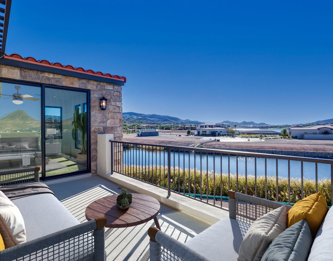 A cozy outdoor patio with comfortable seating overlooks a scenic landscape of mountains and buildings in the distance under a clear blue sky.
