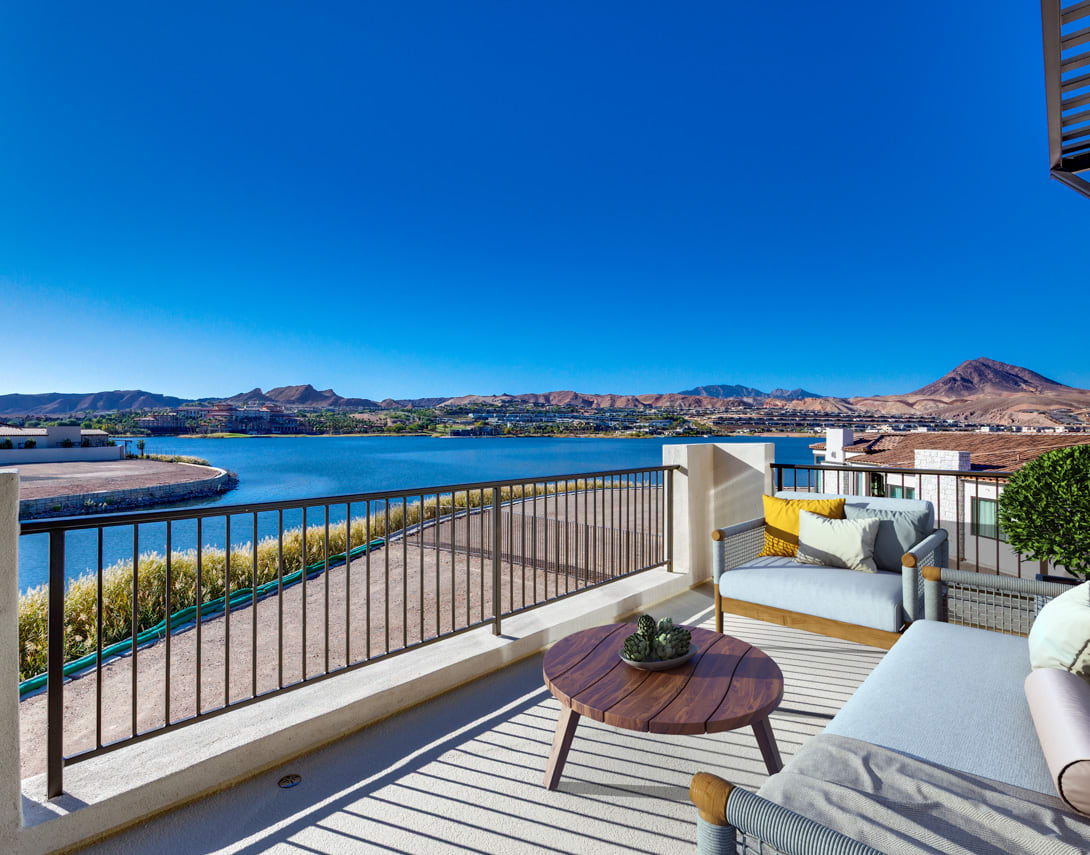 A balcony overlooking a scenic lake surrounded by mountains, with comfortable outdoor furniture and a wooden table in the foreground.
