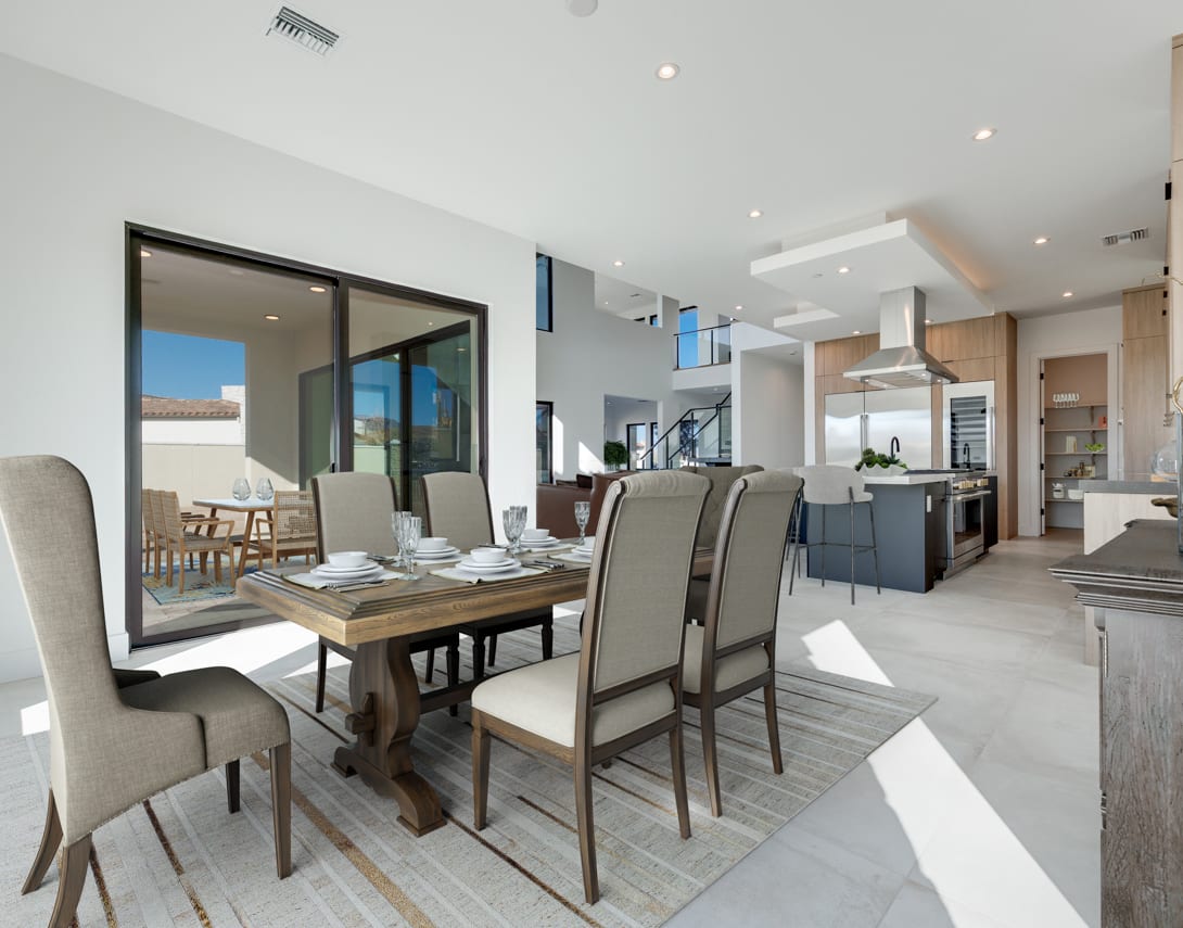 A modern and spacious open-concept living and dining area with a wooden dining table, upholstered chairs, and a kitchen visible in the background.