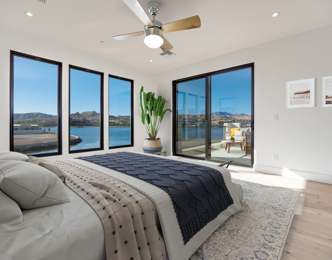 A spacious and modern bedroom with large windows overlooking a scenic outdoor landscape, featuring a comfortable bed, a ceiling fan, and a potted plant.