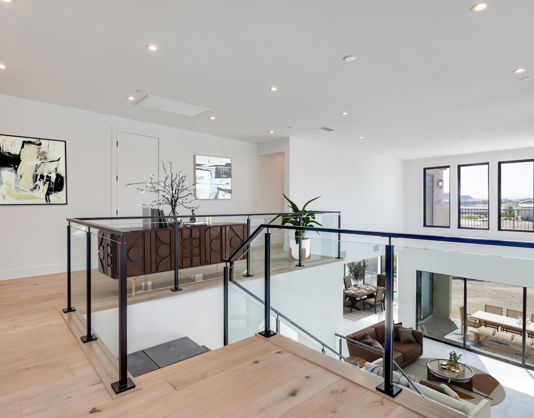 A modern, open-concept living space with a glass-enclosed second floor, wooden floors, and various decorative elements such as artwork and potted plants.