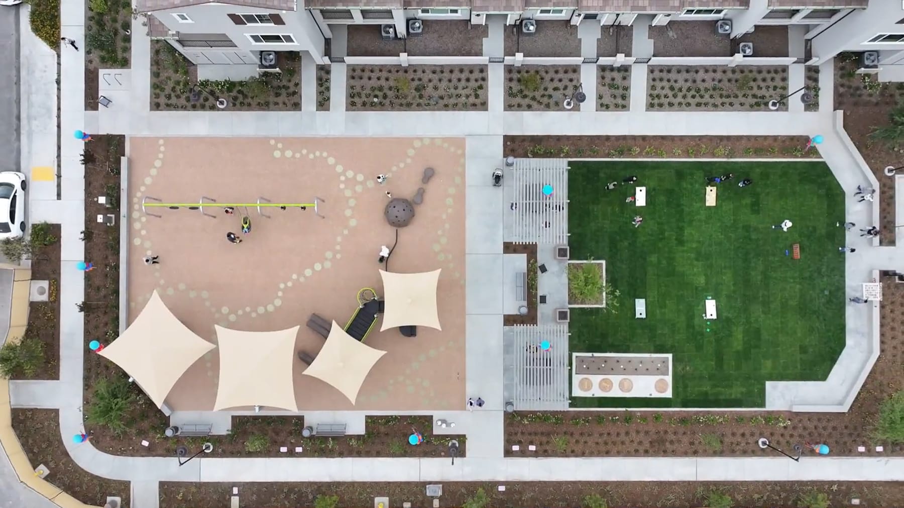 The image shows an outdoor area with a large, abstract sculpture in the foreground and a grassy lawn with various structures and landscaping elements in the background.