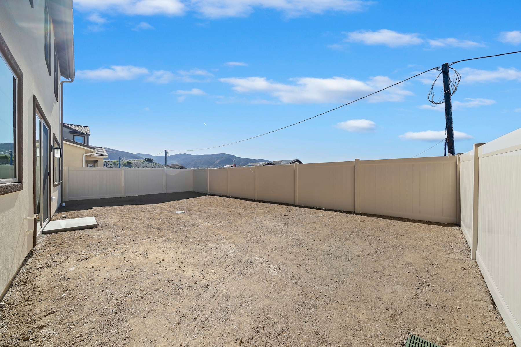 A paved walkway leads through a fenced outdoor area, with a clear blue sky and distant mountains visible in the background.