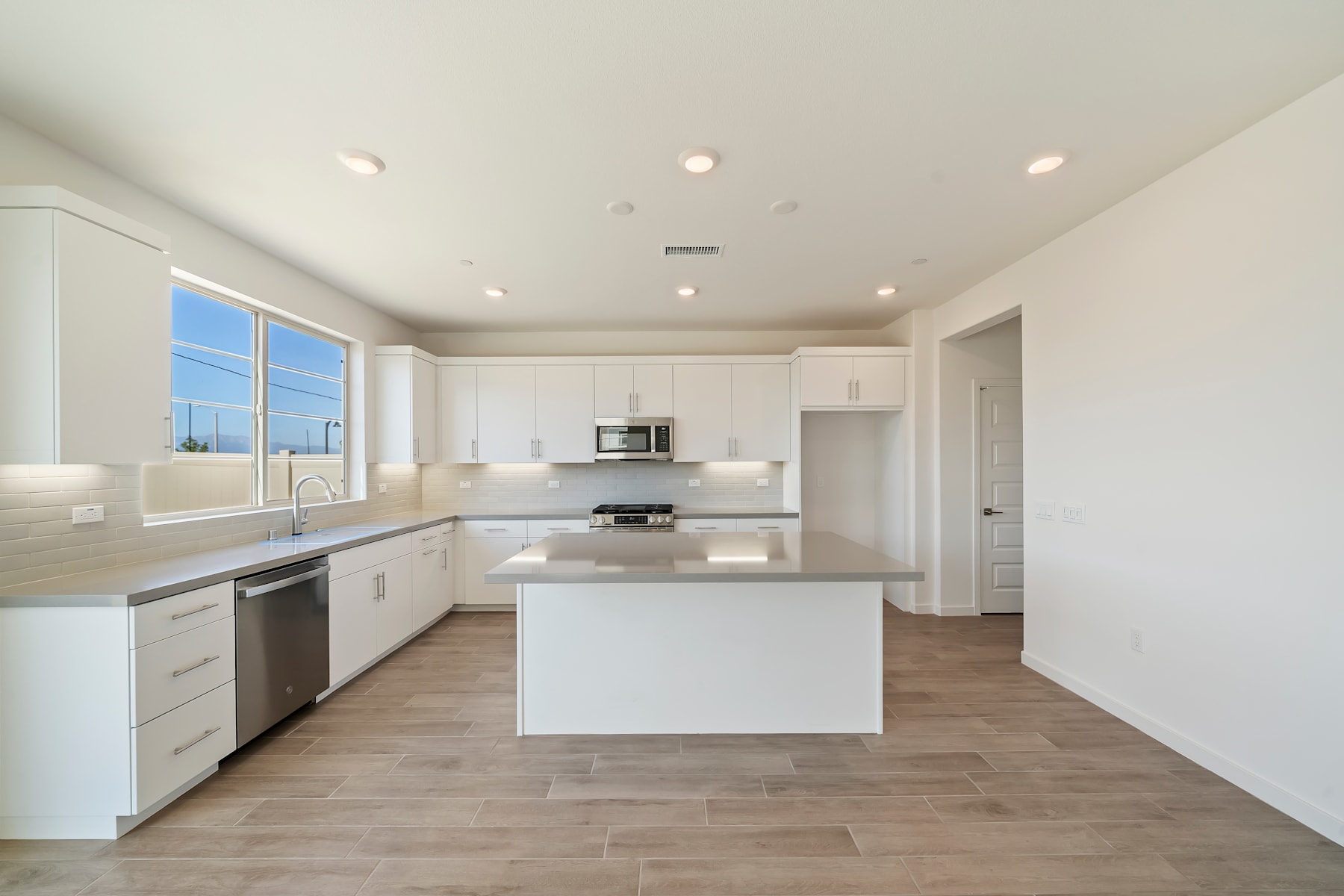 A modern, open-concept kitchen with white cabinets, stainless steel appliances, and a large central island with a wooden floor.