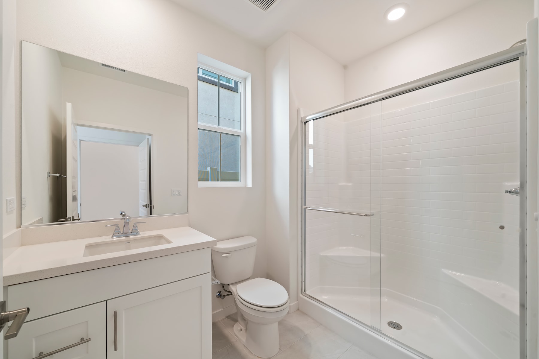 A modern, well-lit bathroom with a vanity, toilet, and a shower enclosure, featuring clean, minimalist design elements.