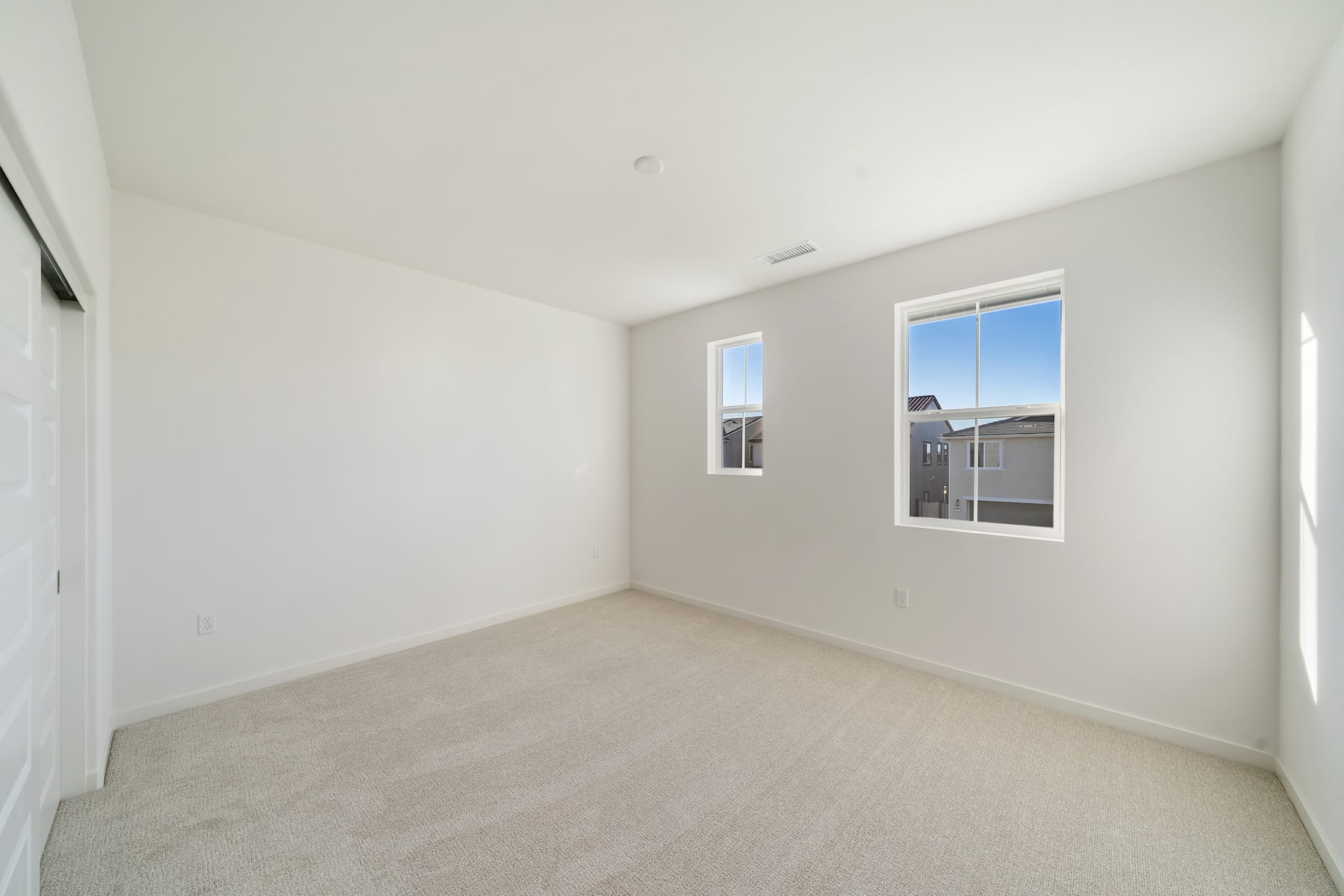 A bright, empty room with white walls, a window, and a carpeted floor.
