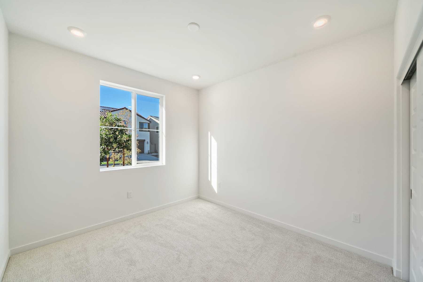 A bright, empty room with a large window overlooking a lush, green outdoor scene.