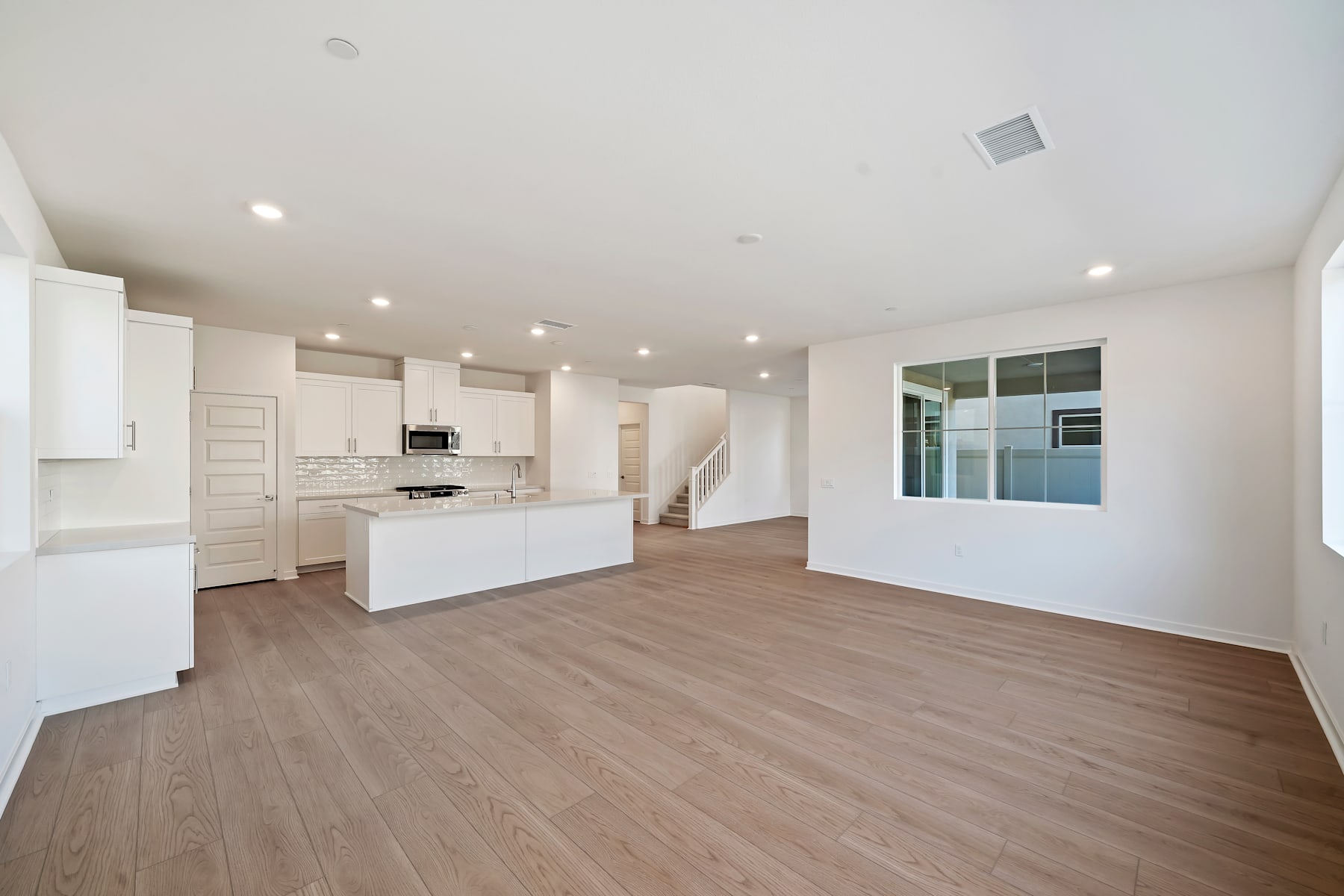 A spacious, open-concept living area with a modern kitchen, hardwood flooring, and large windows allowing natural light to fill the space.