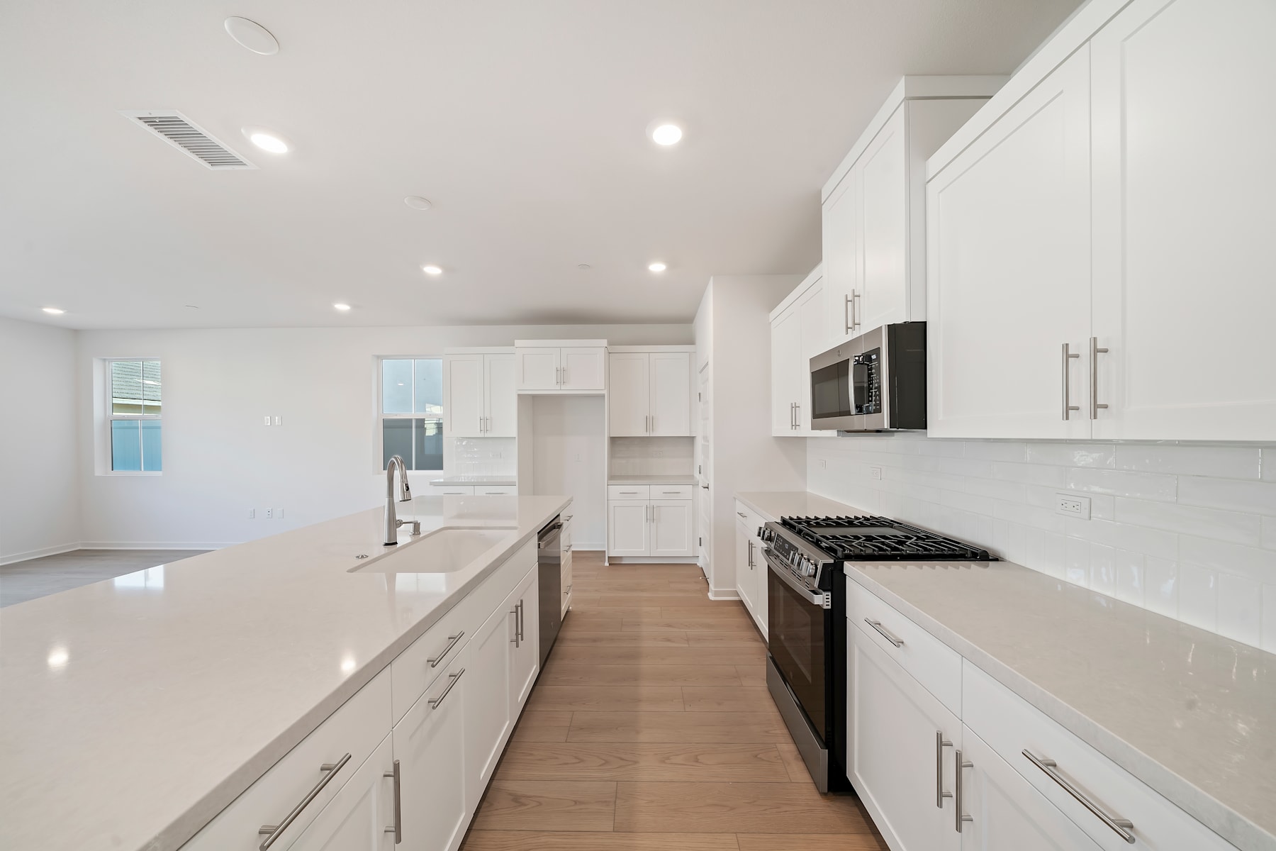 A modern, bright, and spacious kitchen with white cabinets, stainless steel appliances, and a long countertop extending along the room.