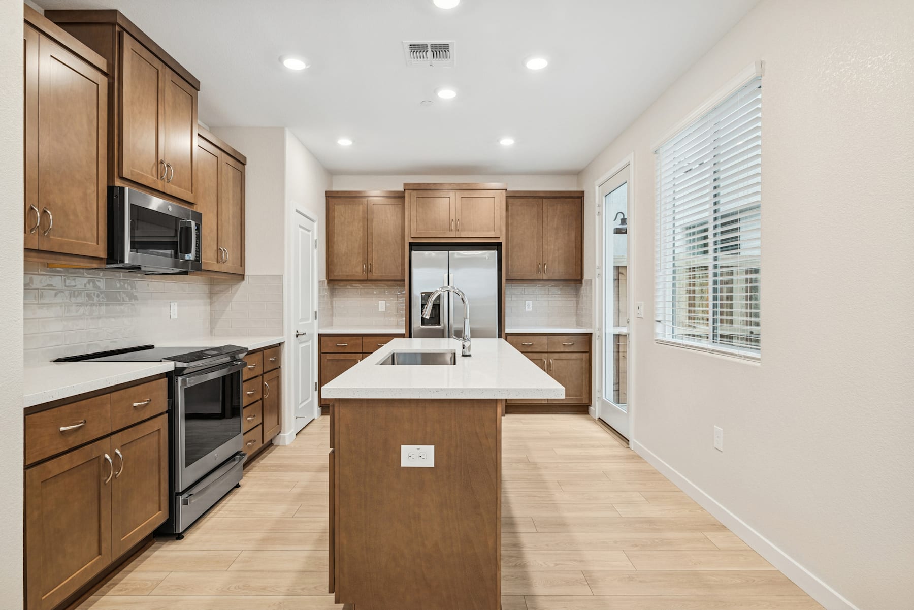 A modern, well-equipped kitchen with wooden cabinets, stainless steel appliances, and a central island with a white countertop.