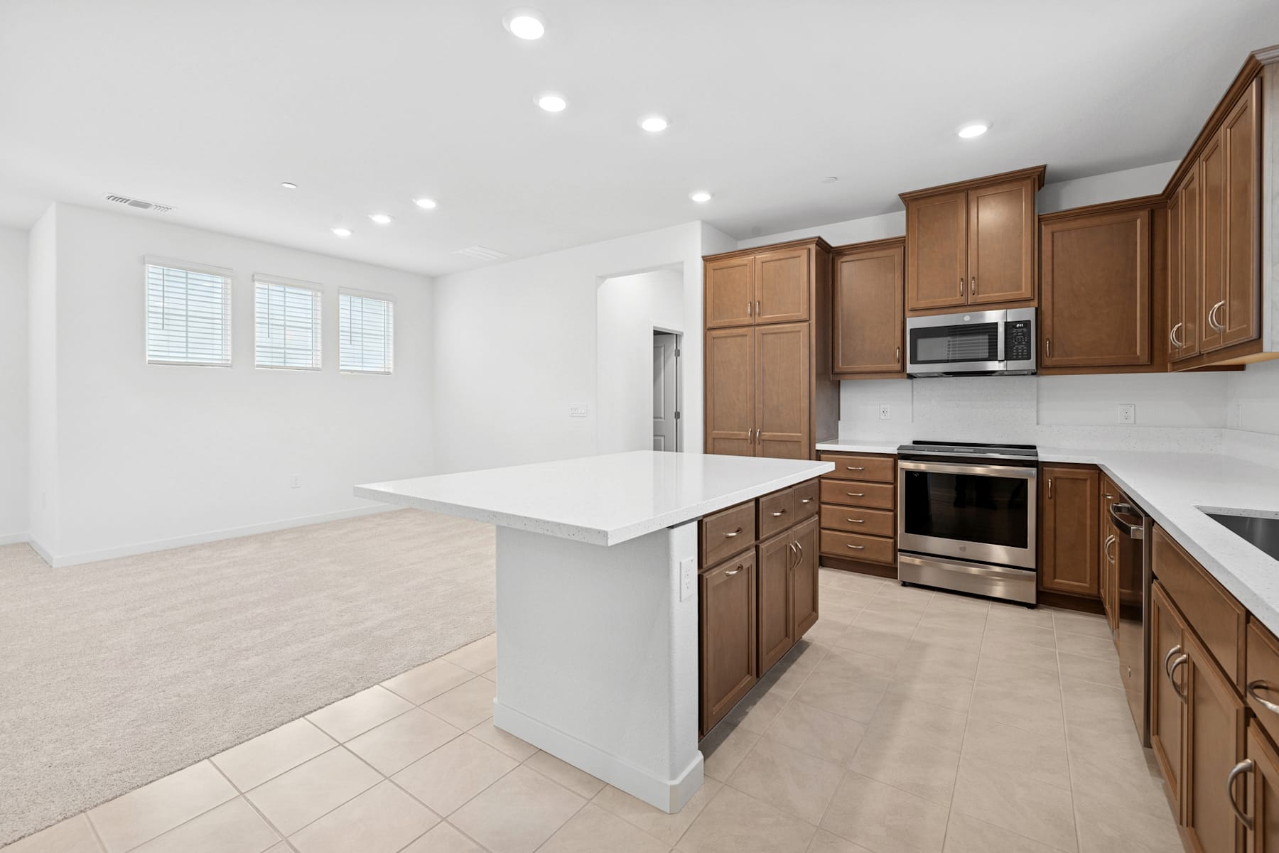 A modern, well-lit kitchen with wooden cabinets, stainless steel appliances, and a white countertop island in the foreground.