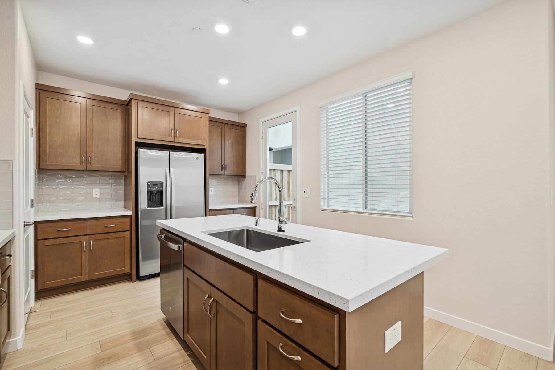 A modern kitchen with wooden cabinets, a white countertop, and stainless steel appliances, set against a bright and airy background.