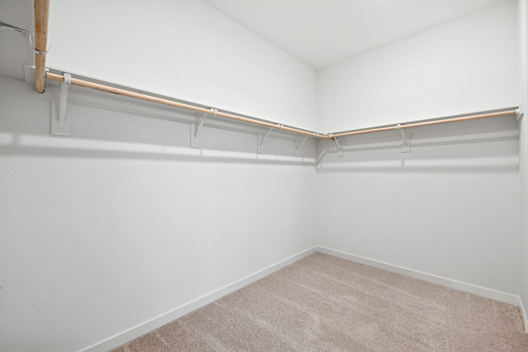 A spacious, well-lit closet with white walls, a carpeted floor, and metal clothing rods installed along the corners.
