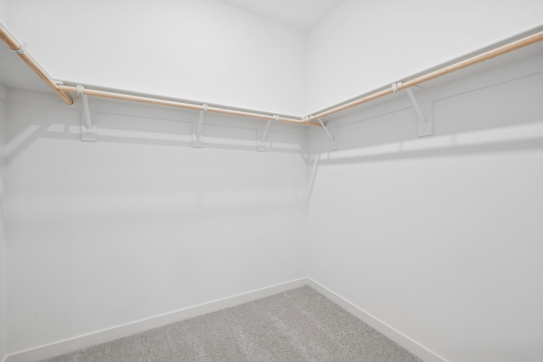 A white, empty closet with wooden shelves and rods, providing ample storage space.